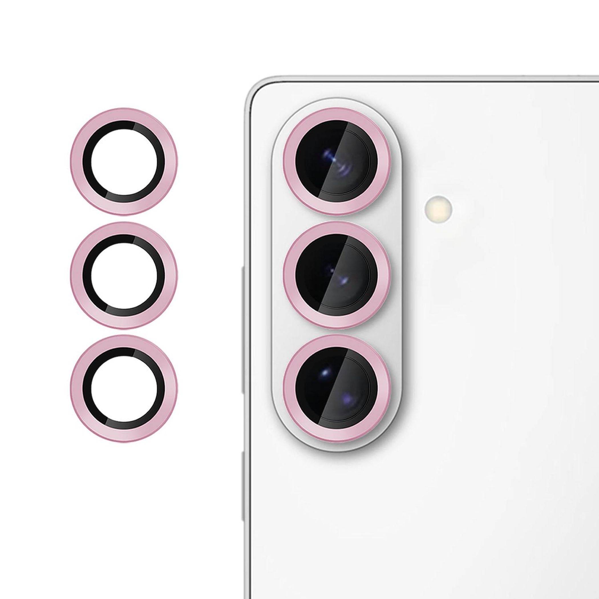 Weißes Smartphone, von hinten gezeigt, mit einem Triple-Kamera-Modul. Drei rosa Kameralinsenringe sind separat auf der linken Seite angezeigt und zeigen Schutzabdeckungen für die Kamera an.