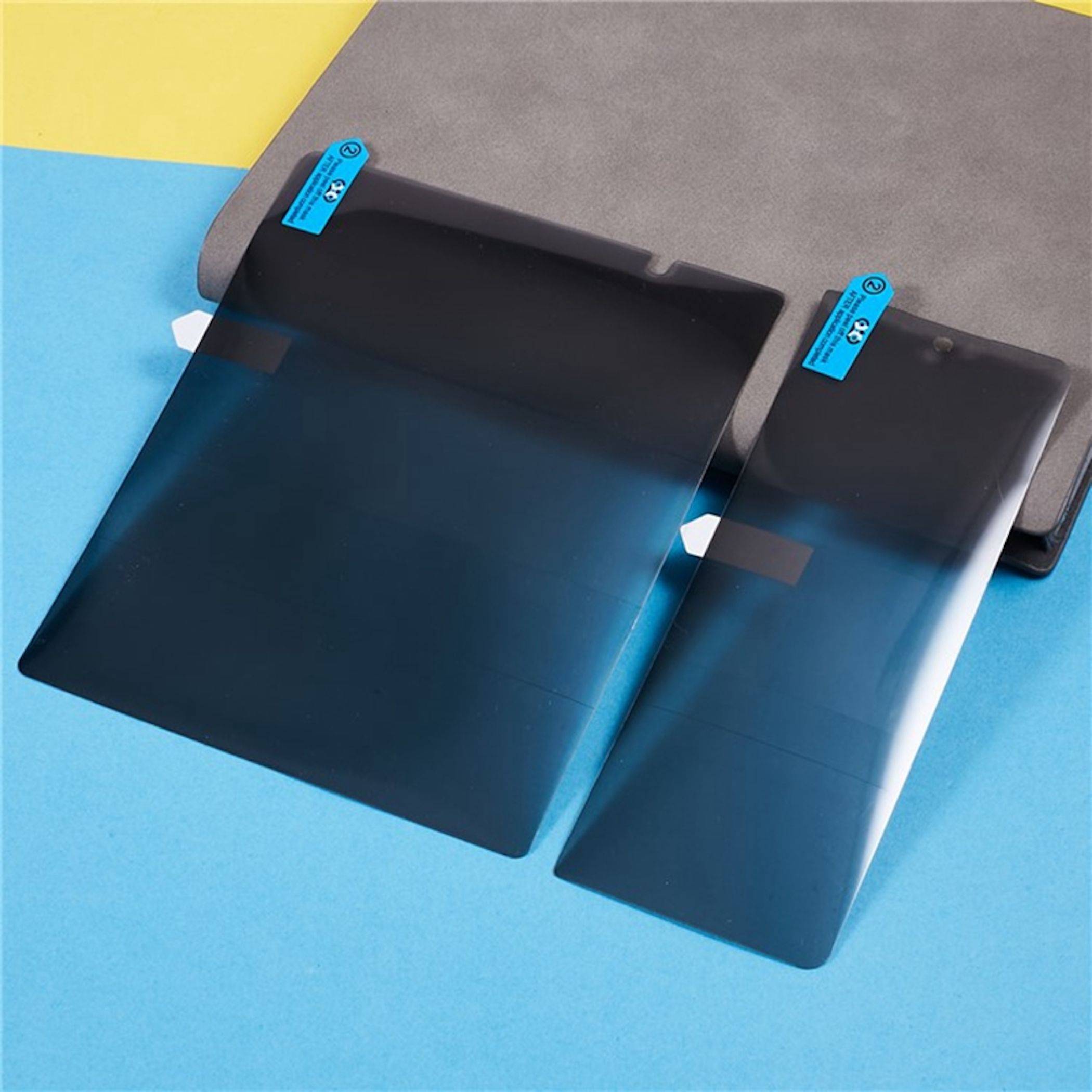 Zwei dunkelblaue Gradientenschutzfolien oder Handyfolien liegen auf einer blaugrauen Oberfläche, jede mit einem kleinen blauen Abziehtab oben.