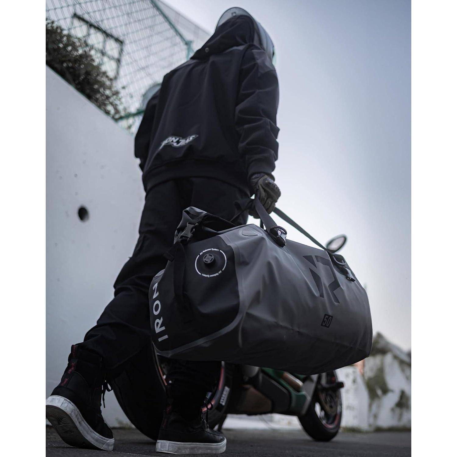 Person in schwarzem Hoodie und Maske, der eine große Reisetasche trägt, während er neben einem Motorrad im Freien spaziert.