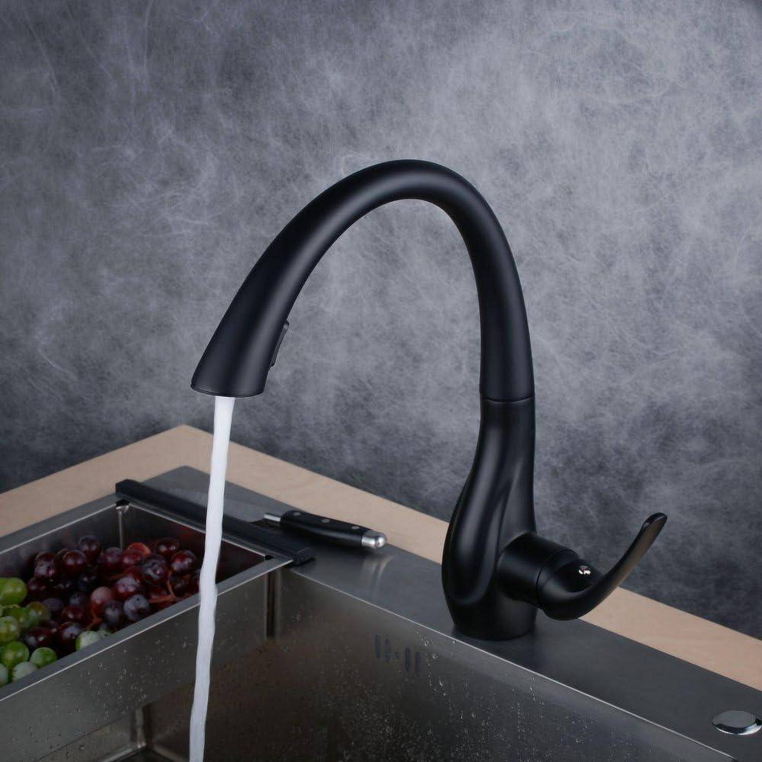 Schwarzer Küchenarmatur, aus dem Wasser in ein Waschbecken neben einem Tablett mit Trauben auf der Arbeitsplatte fließt.