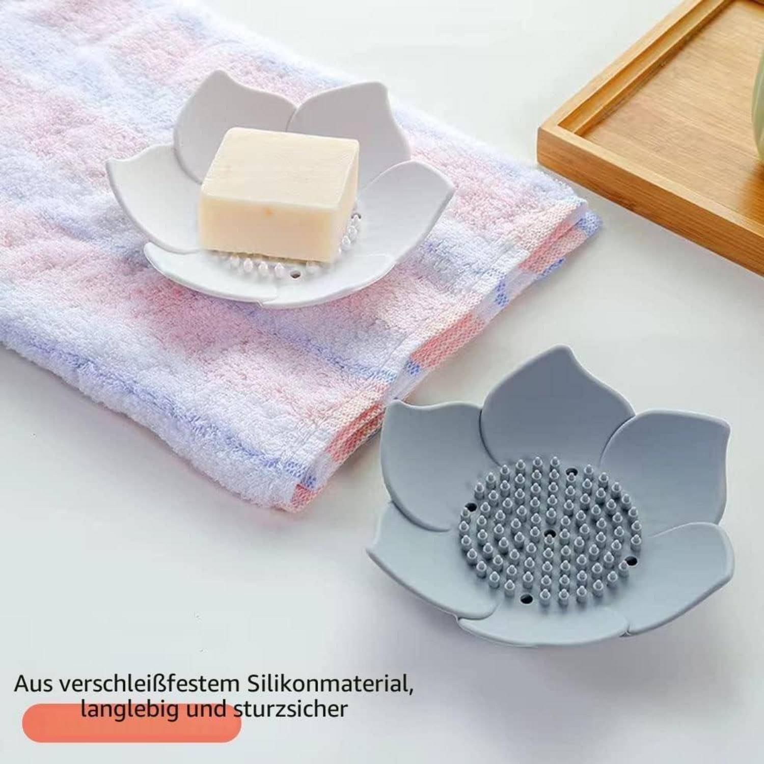 Zwei blumenförmige Silikon-Seifenschalen, eine mit einem Seifenstück, gezeigt mit deutschem Text über haltbares, rutschfestes, verschleißfestes Material.