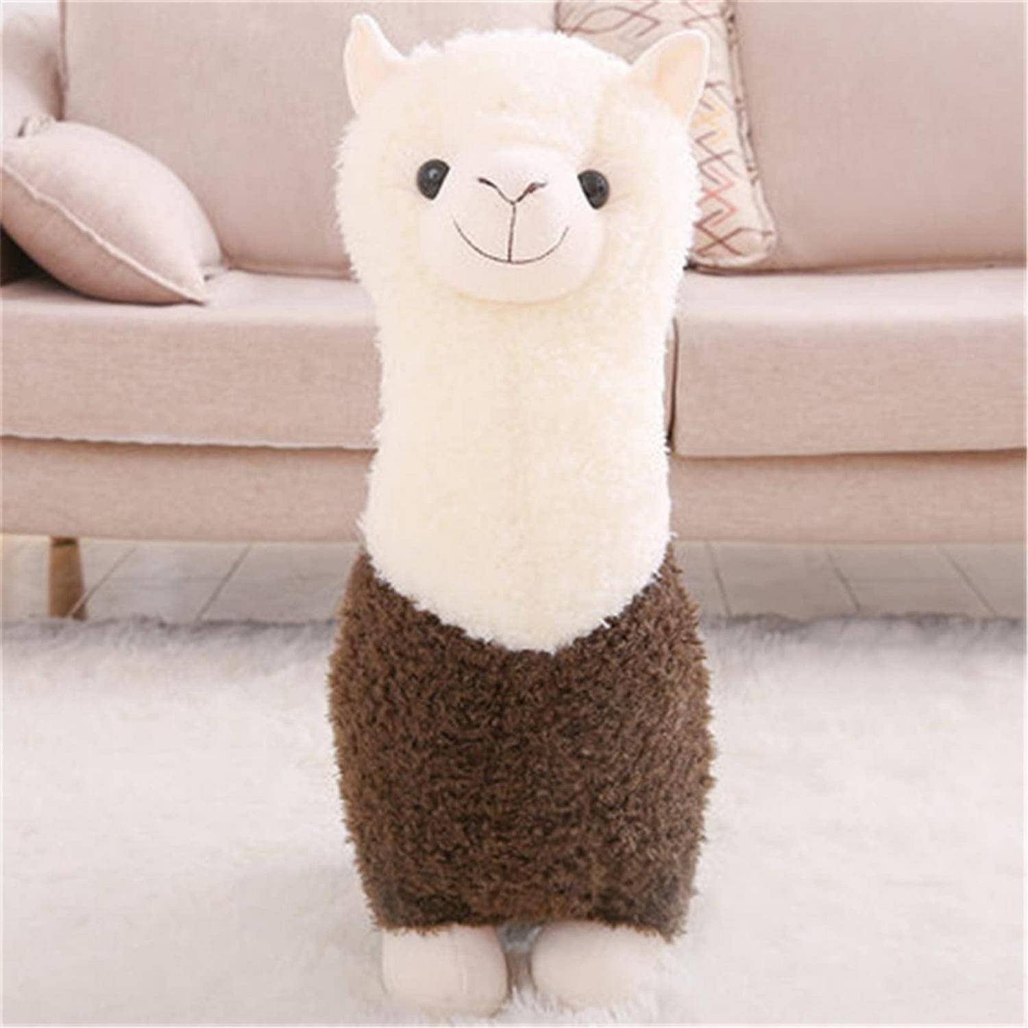 Ein kuscheliges Lama-Spielzeug mit weißem Kopf und braunem Körper steht auf einem flauschigen Teppich vor einem beigefarbenen Sofa.
