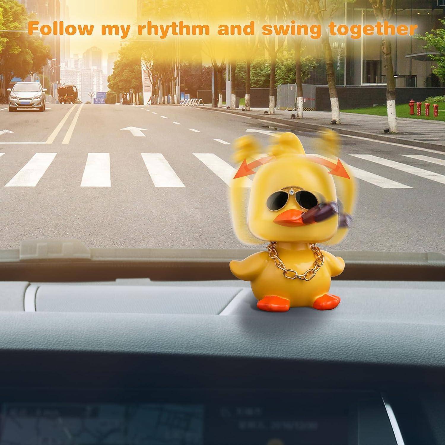 Eine kleine gelbe Tanzenten-Figur mit Sonnenbrille auf einem Auto-Armaturenbrett, mit Text der besagt „Folge meinem Rhythmus und schwinge zusammen" über einer Straßenansicht.