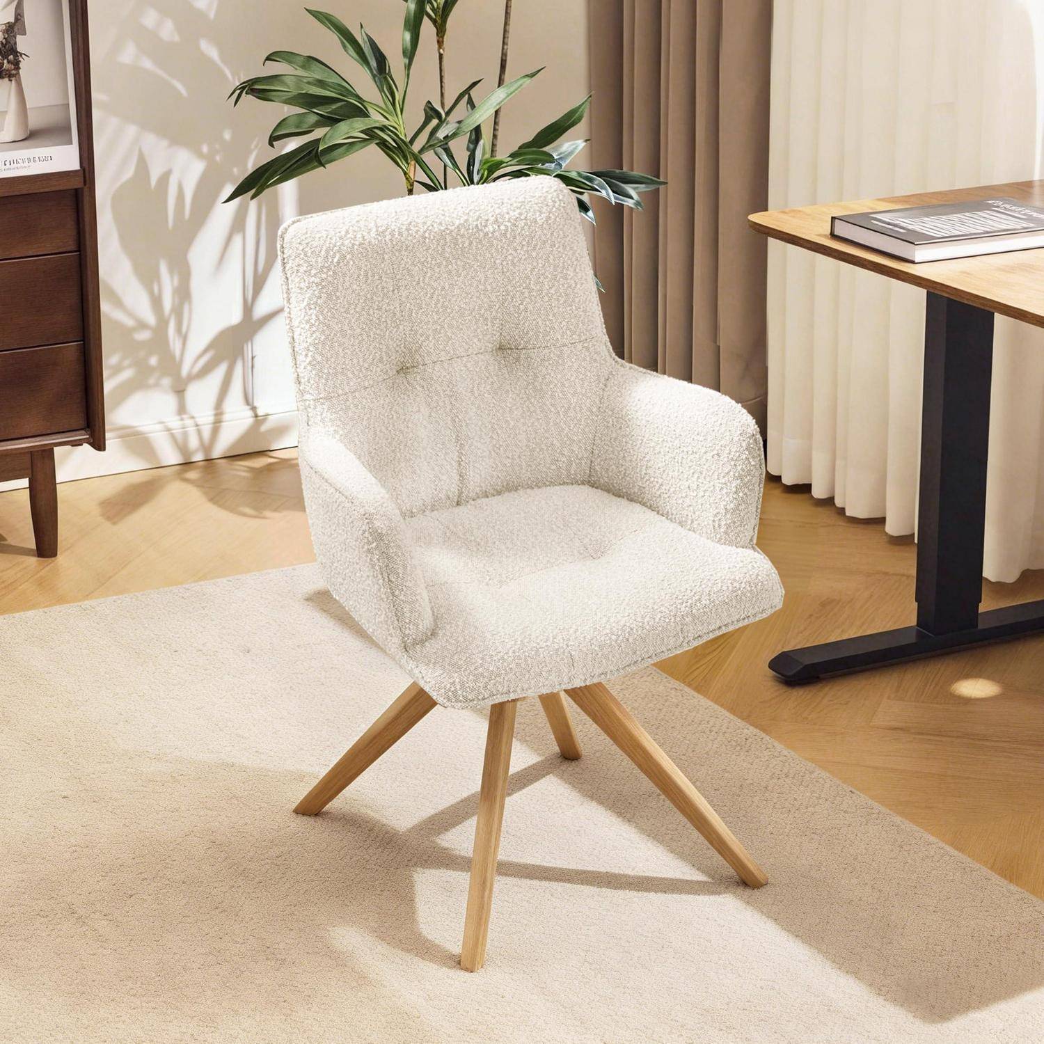 Weißer gepolsterter Sessel mit Holzbeinen steht auf einem beigen Teppich in einem hellen Raum neben einem Tisch und einer Pflanze.