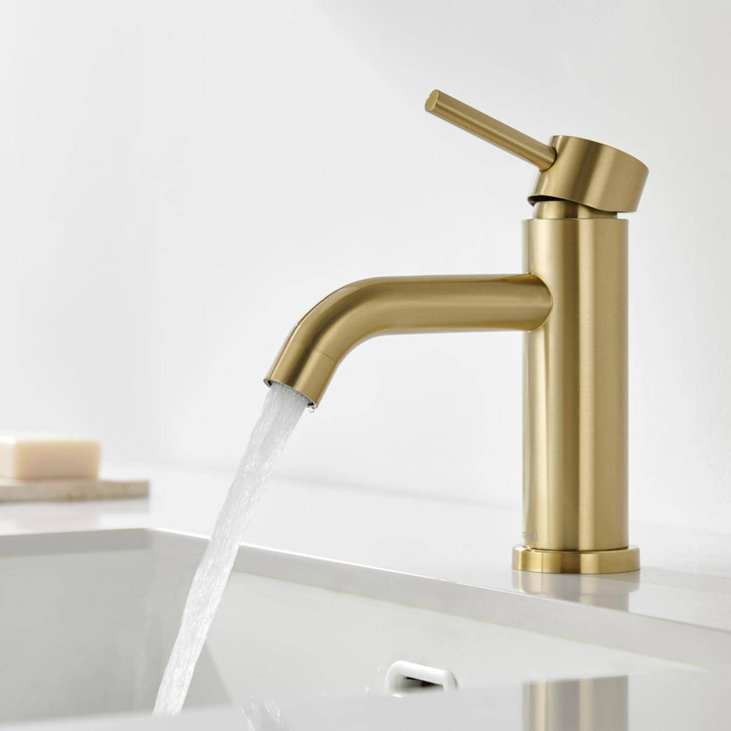 Goldfarbener Badezimmerhahn mit fließendem Wasser in ein weißes Waschbecken vor minimalistische weißem Hintergrund.