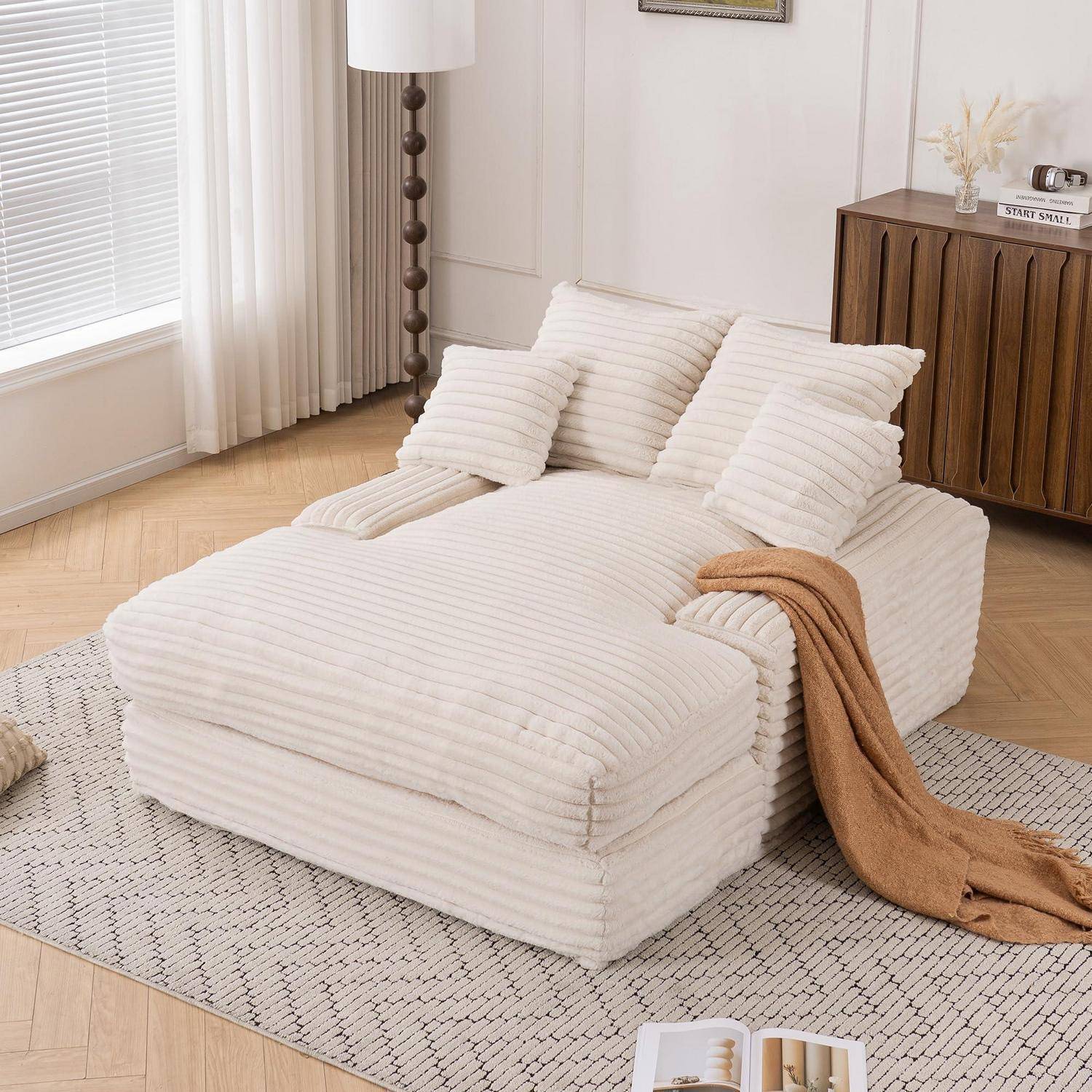 Ein weißes Kordsamtsofabett mit passenden Kissen und einer beigen Wurfdecke, angeordnet in einem hellen minimalistischen Wohnzimmer.