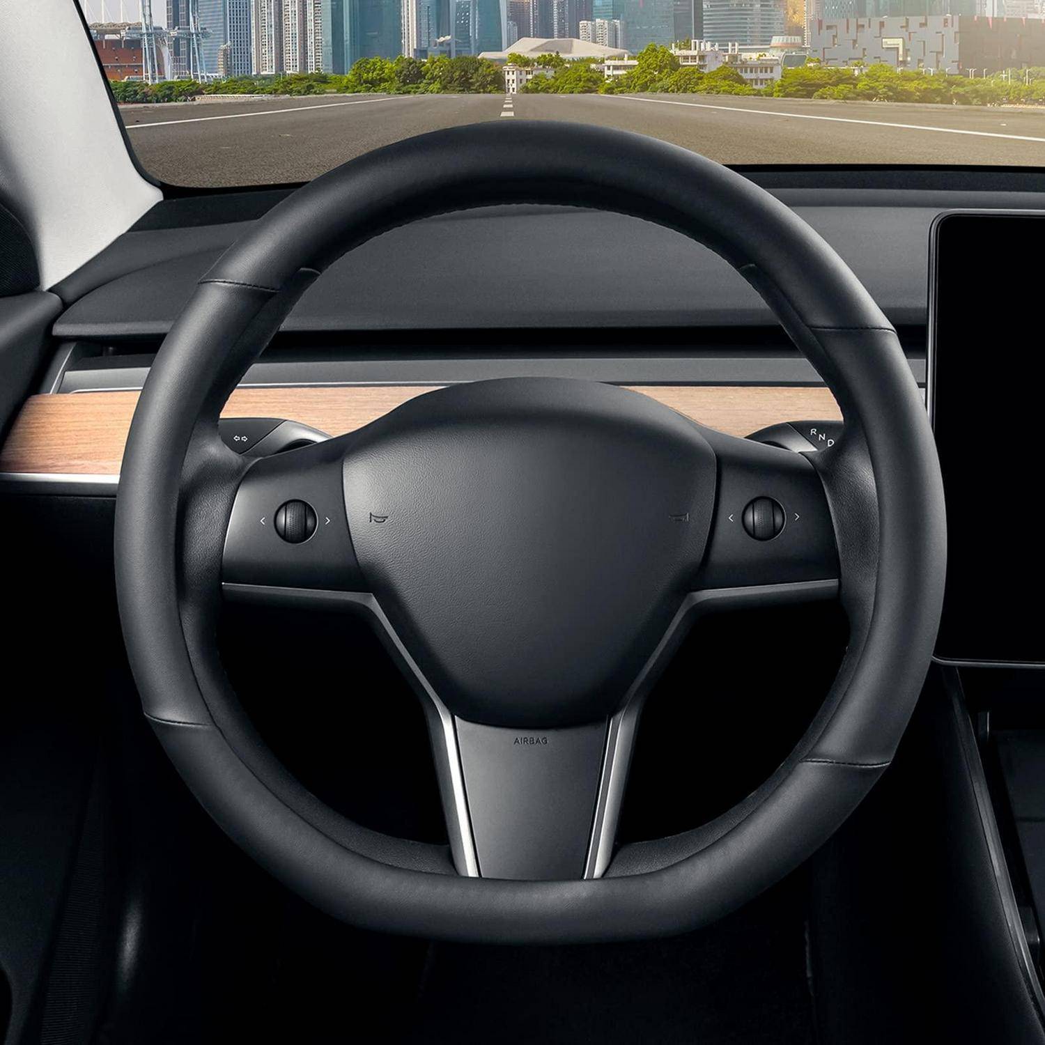 Blick ins Innere eines Autos, zentriert auf ein schwarzes Lenkrad mit einem minimalistischen Armaturenbrett und der Straße vor uns, die durch die Windschutzscheibe sichtbar ist.