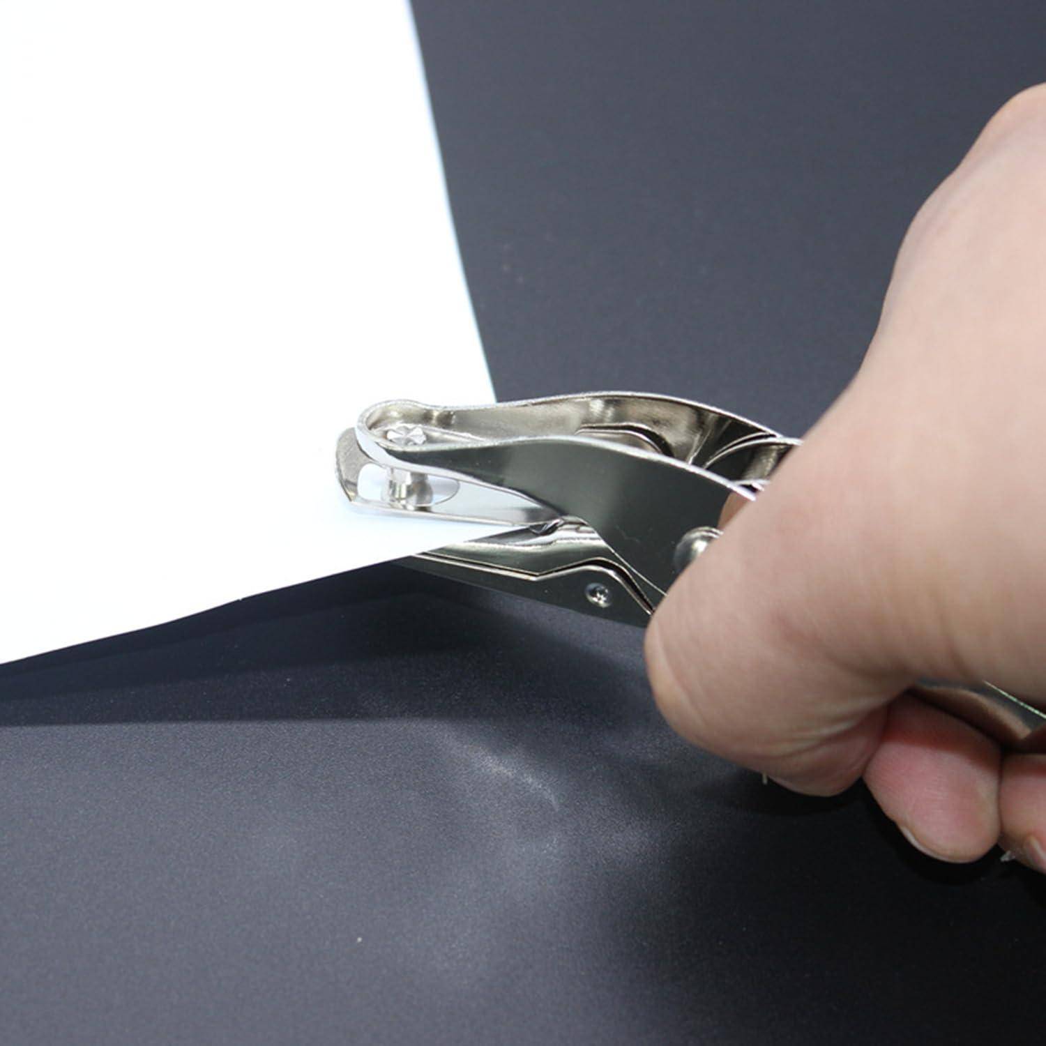 Hand benutzt eine Metall-Lochzange auf einem schwarzen Blatt Papier über einem weiß-dunklen Hintergrund.