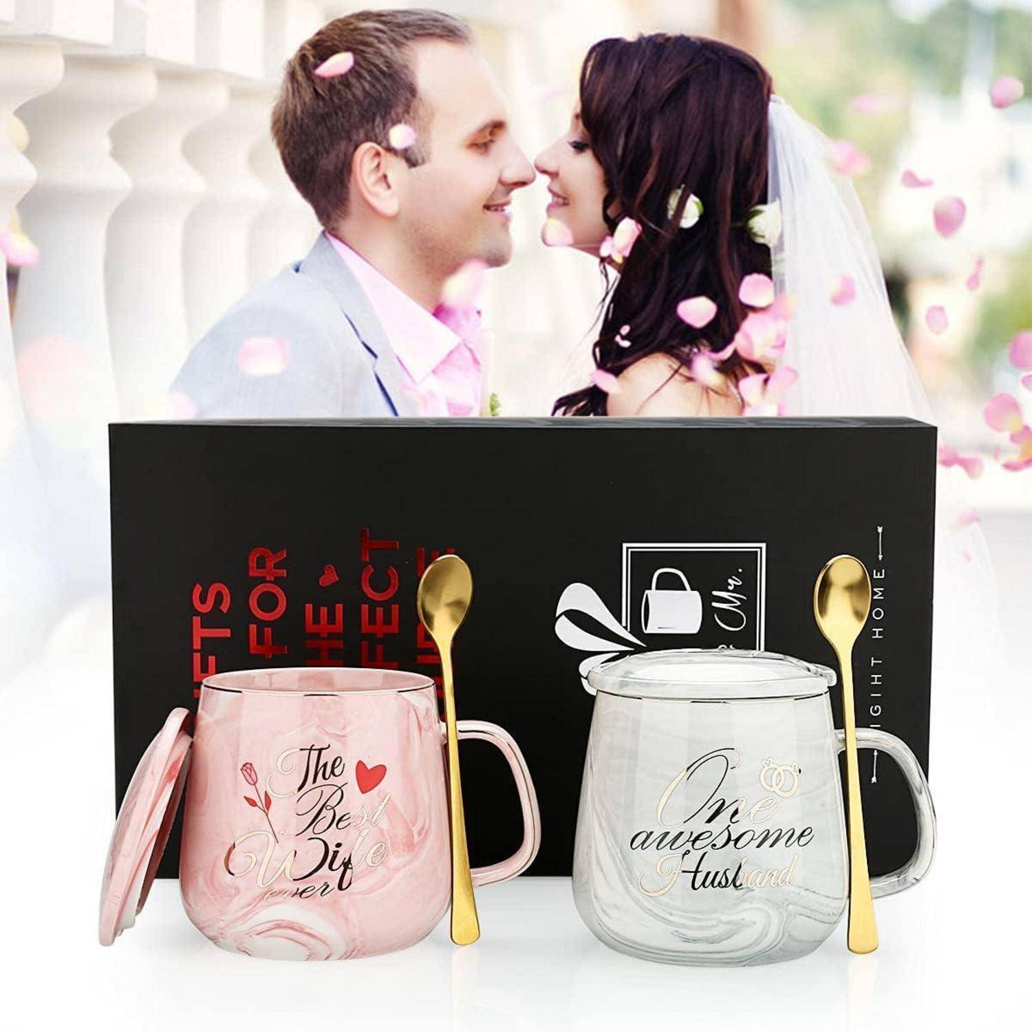 Geschenkset aus zwei Glastassen mit goldenen Löffeln in Rosa- und Klartönen mit Marmor-Design, gezeigt mit romantischem Paarhintergrund und schwarzer Präsentationsbox.