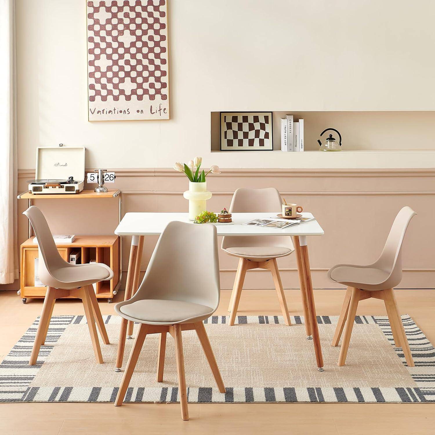 Modernes Esszimmer mit weißem Tisch und vier beigen Stühlen auf einem gemusterten Teppich, mit Wandkunst und einem Regal in einem weich neutralen Innenraum.