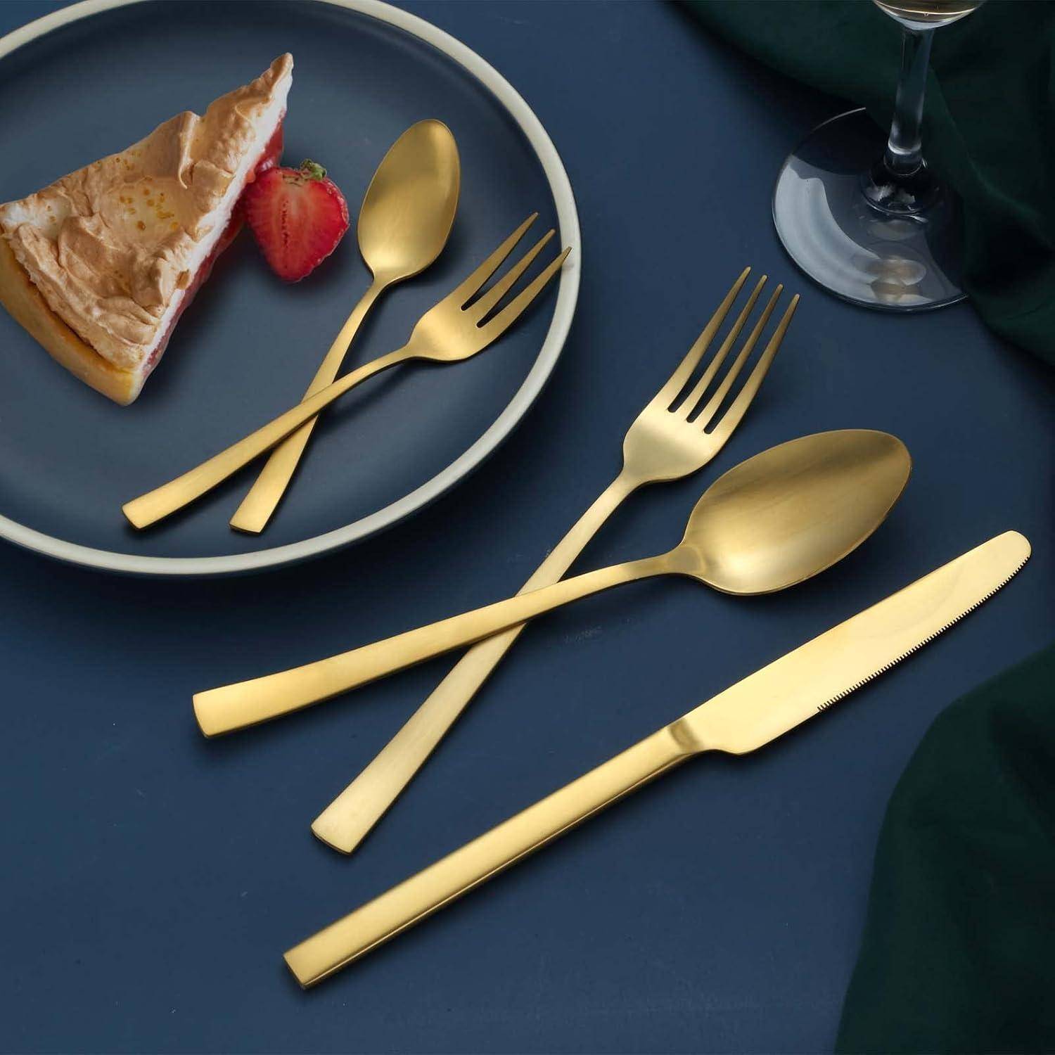 Goldfarben besteck auf einem dunkelblauem Tisch neben einem Dessertteller mit Kuchen und Erdbeere arrangiert.