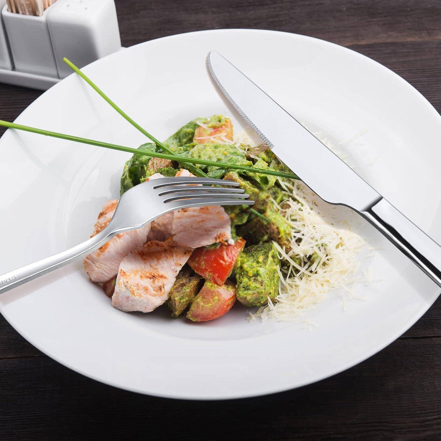 Weißer Teller mit geschnittenem Hähnchen, Avocado- und Tomatensalat, belegt mit geriebenem Käse; Gabel, Messer und Schnittlauch obenauf.