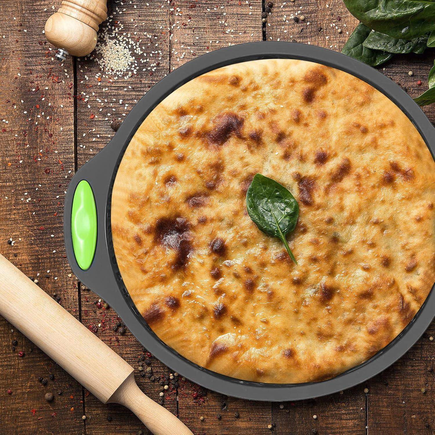 Goldbraun gebackene Pizza oder Fladen in einer runden schwarzen Pfanne mit grünem Griff, belegt mit einem Basilikumblatt, auf einem rustikalen Holztisch mit Mehl und einem Nudelholz.