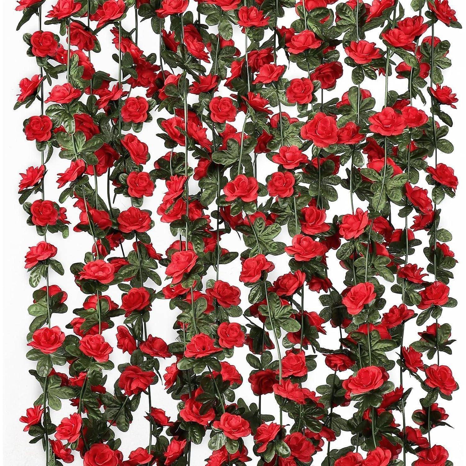 Dichter Vorhang aus roten künstlichen Rosen und grünen Ranken, die vertikal gegen einen weißen Hintergrund hängen.