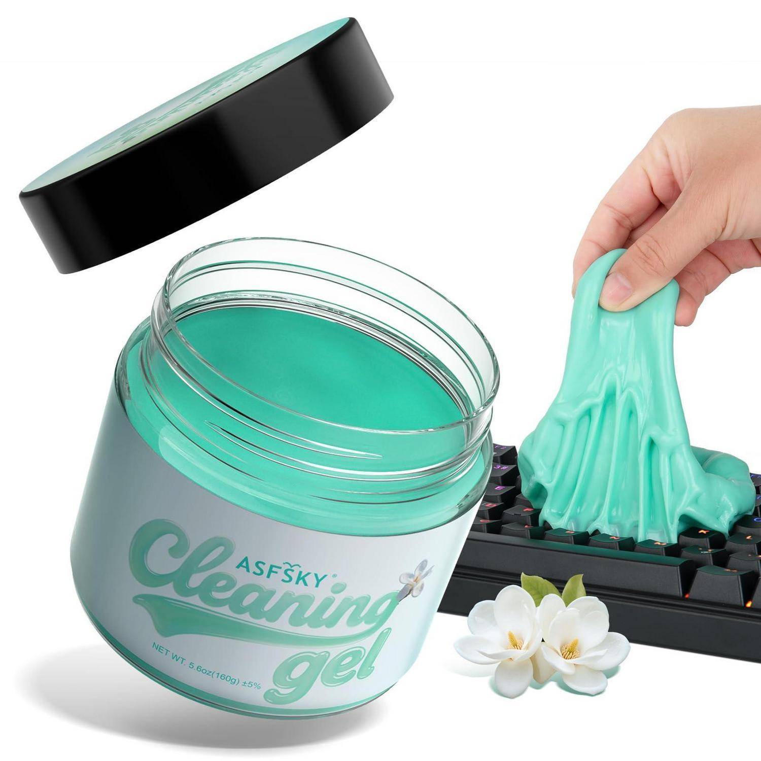 Hand zieht türkises Reinigungsgel aus einer Tastatur neben einem offenen Glas mit der Aufschrift „Reinigungsgel