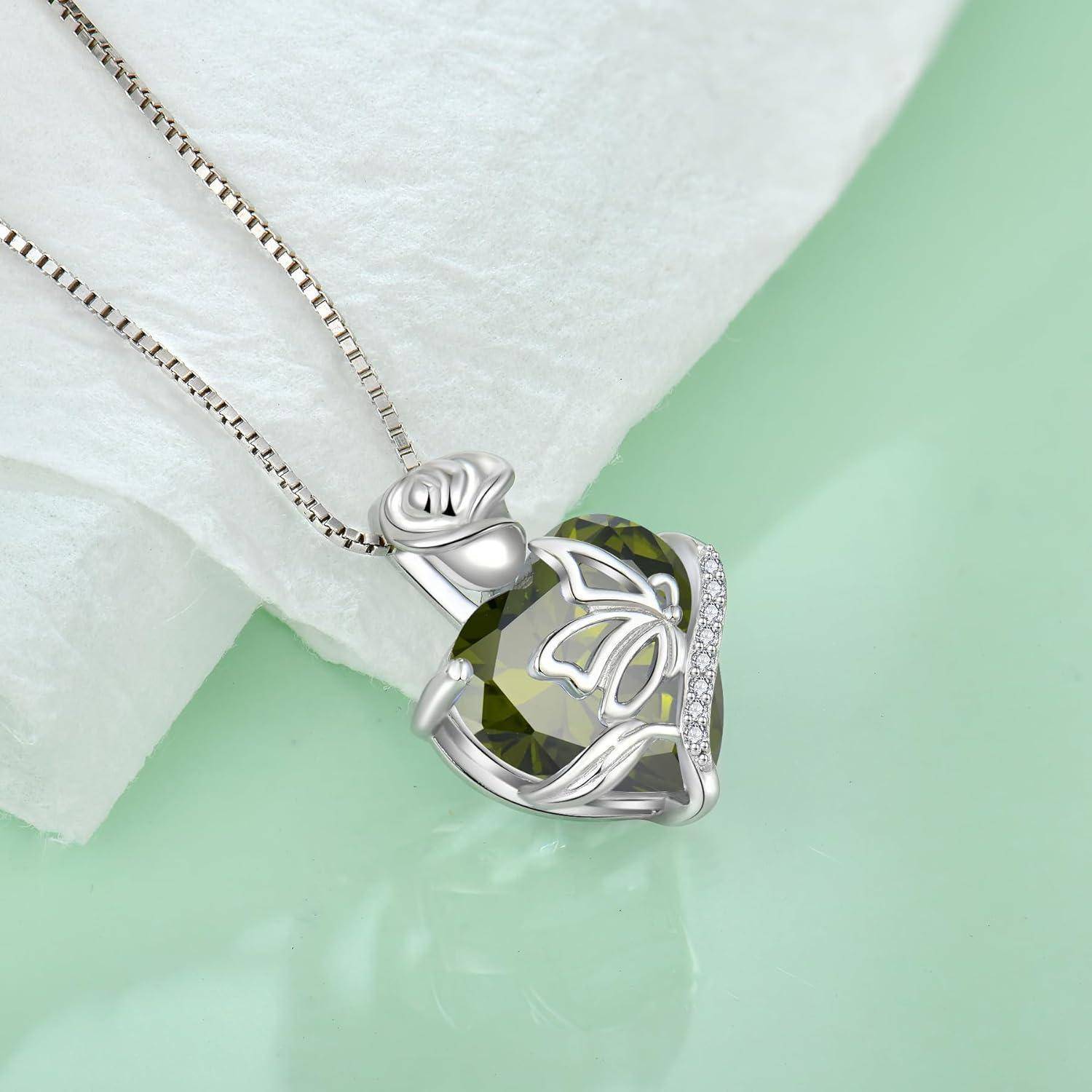 Silberhalskettenanhänger mit einem geschliffenen grünen Edelstein und schmetterlingsähnlichem Design an einer Kette, fotografiert vor einem hellgrünen Hintergrund.
