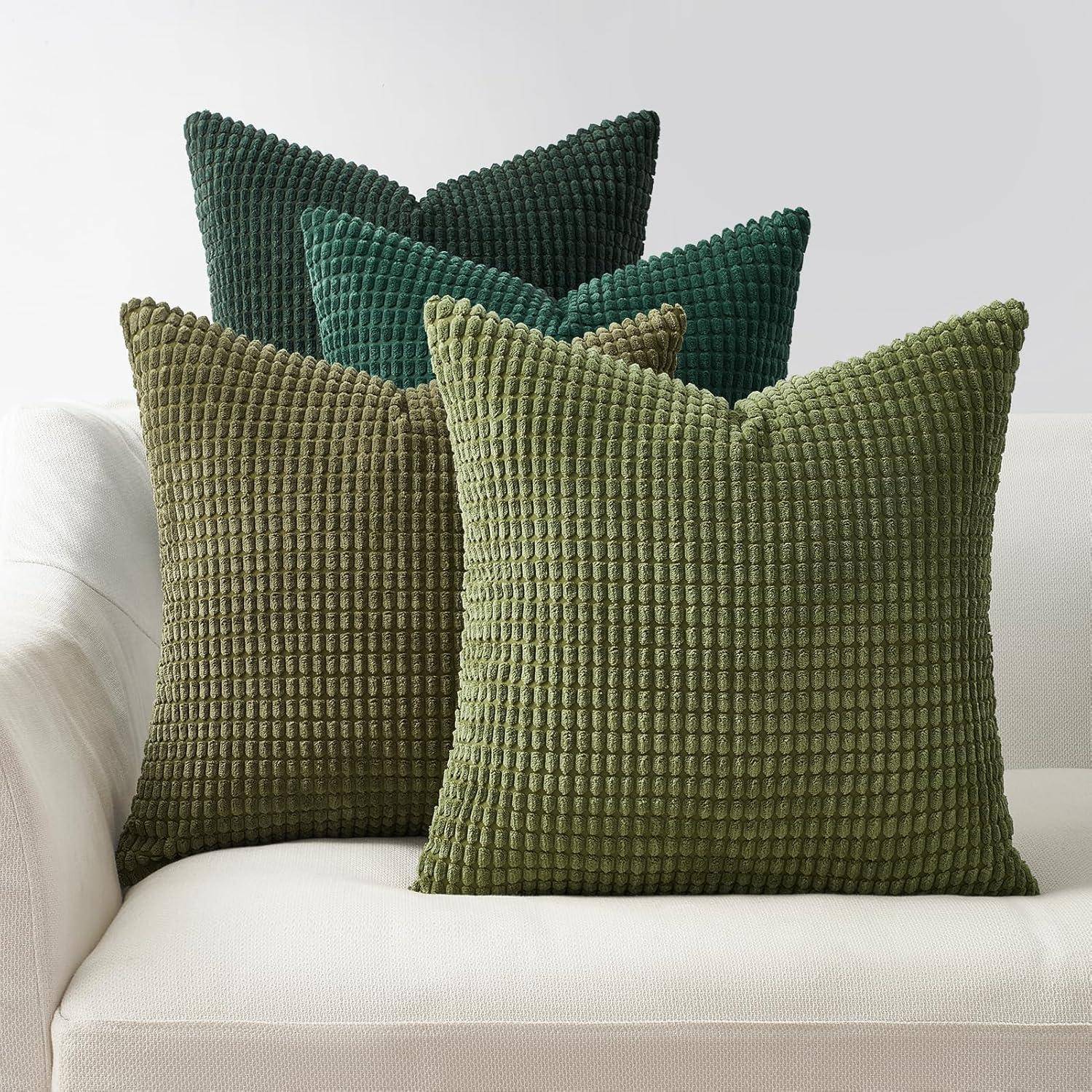 Vier strukturierte grüne Dekokissen auf einem weißen Sofa vor einer hellen Wand arrangiert.