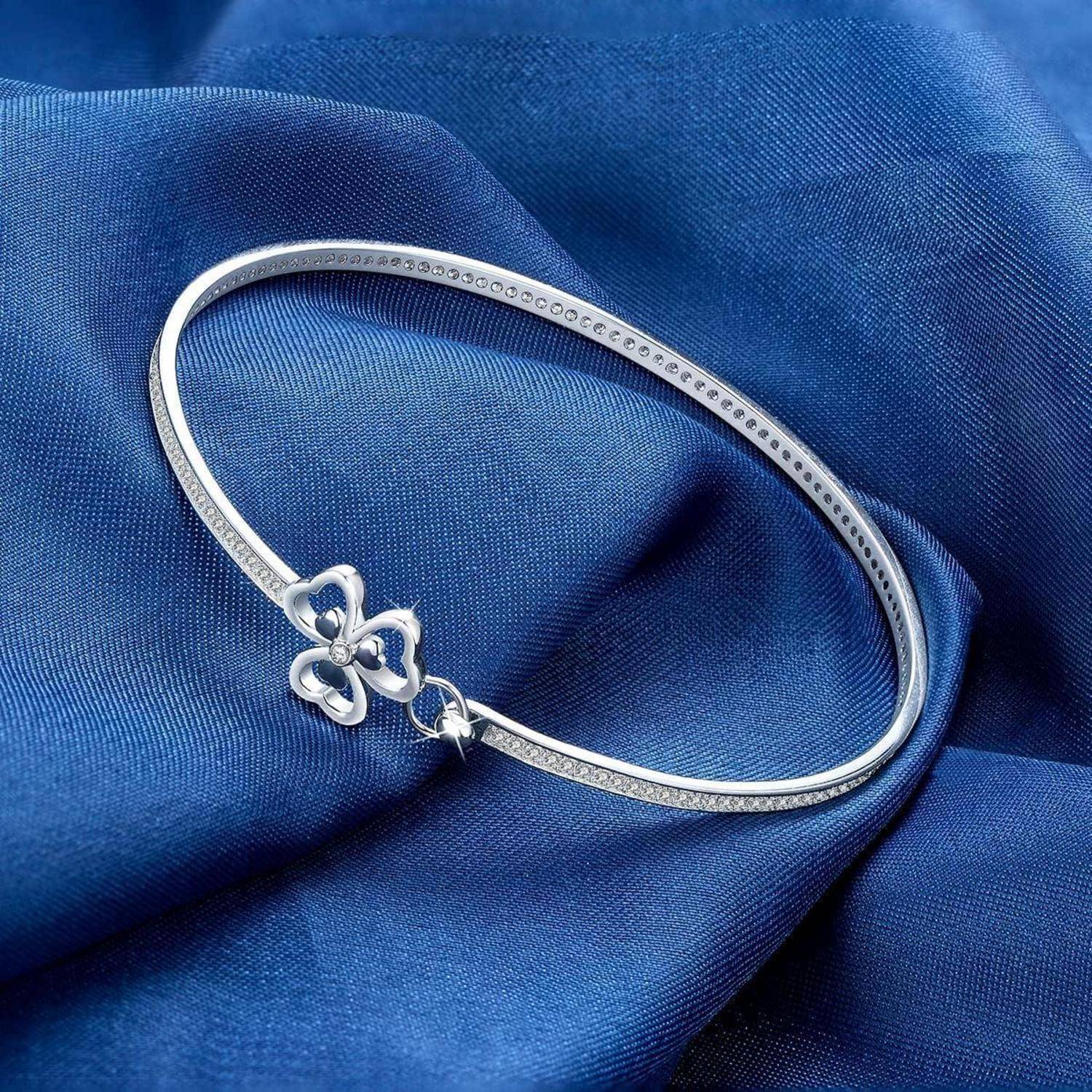 Silbernes ovales Armband mit einem kleinen Kleeblatt-Anhänger auf blauem Stoff.