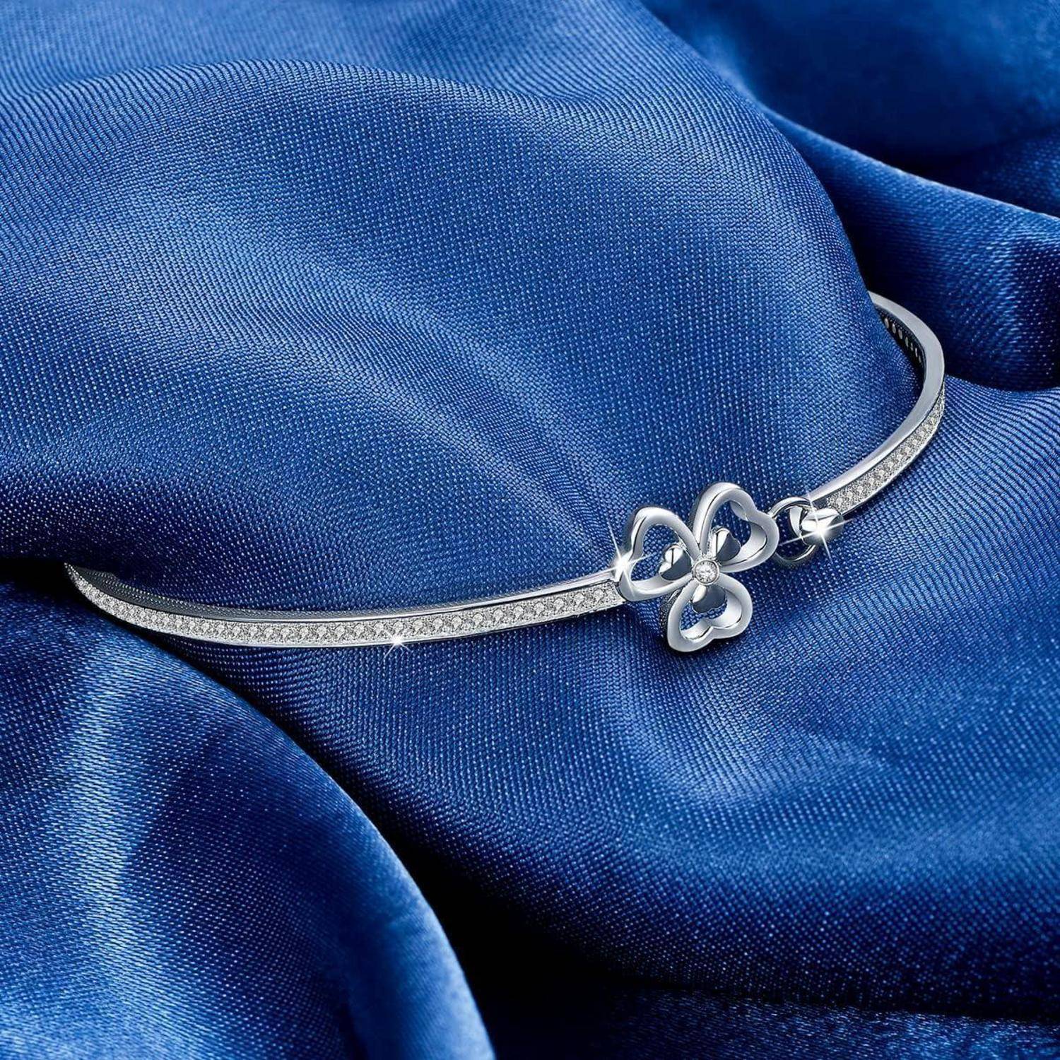 Silbernes Armband mit einem kleeblattförmigen Anhänger auf blauem Satinstoff.
