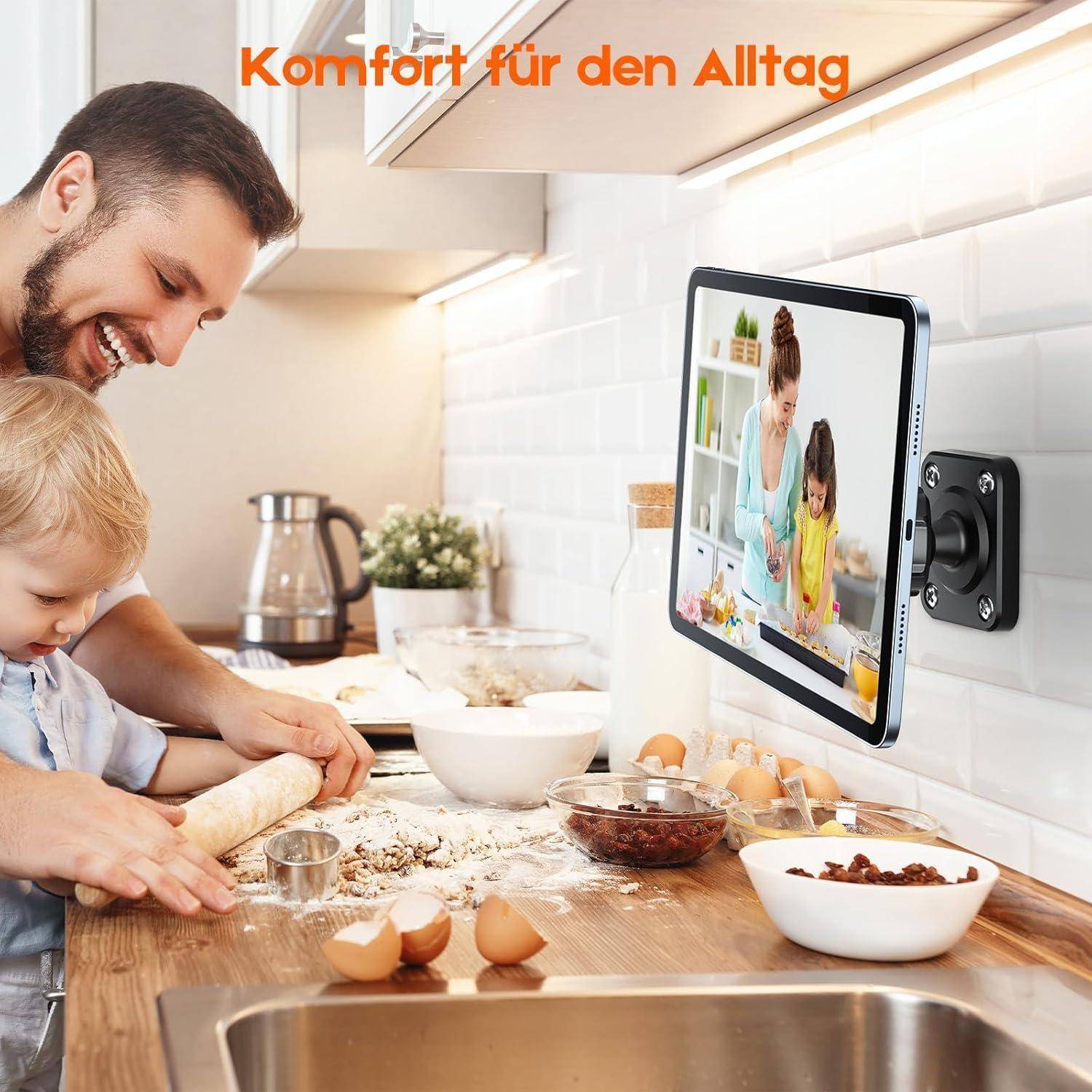 Vater und Kleinkind rollen Teig auf einer Küchentheke, während ein Tablet an einer Wandhalterung ein Kochvideo mit einer Mutter und einem Kind zeigt; der Text lautet "Komfort für den Alltag"".