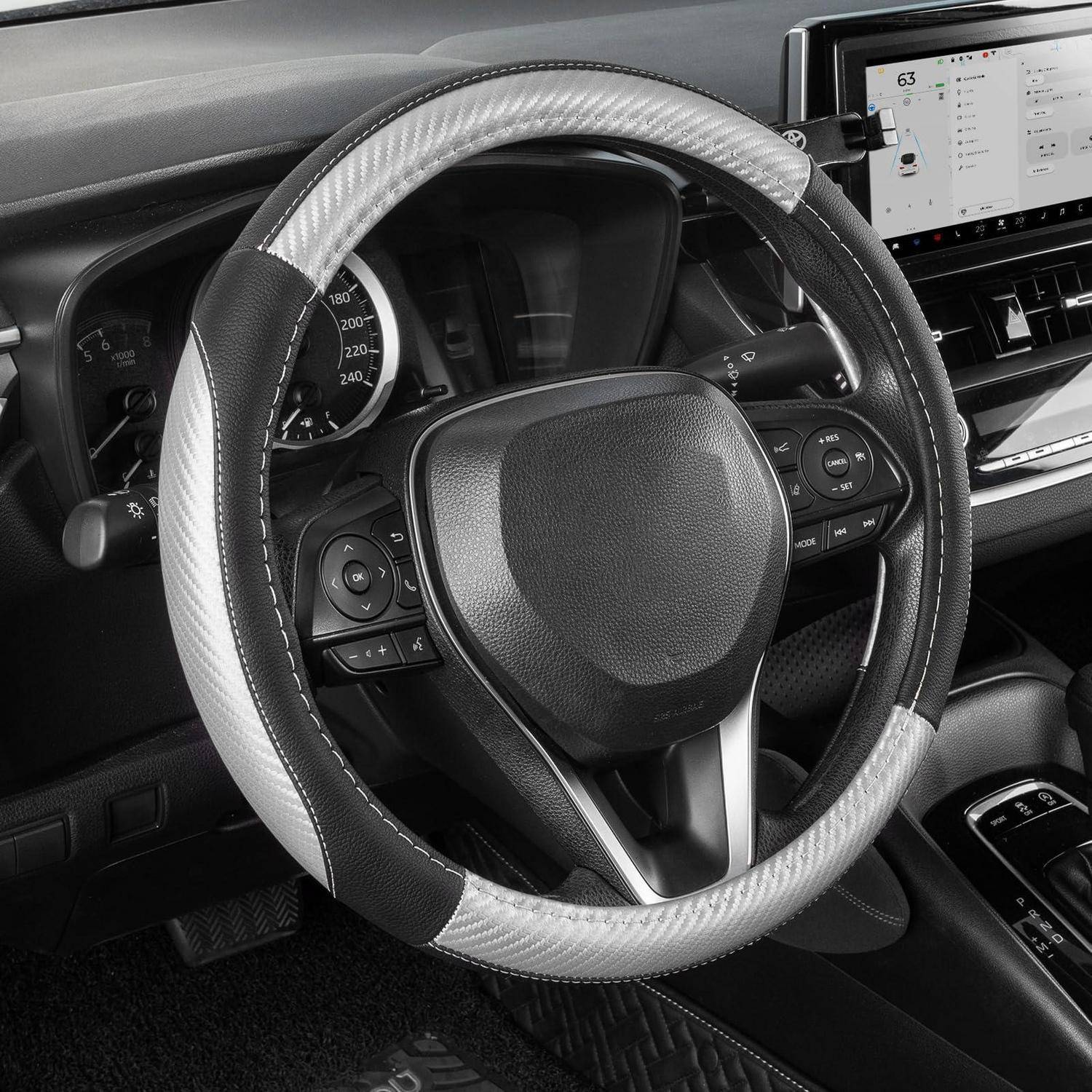 Nahaufnahme eines Autolenkrads mit schwarzweißem Bezug, aus der Fahrersicht neben dem Armaturenbrett und dem Touchscreen fotografiert.