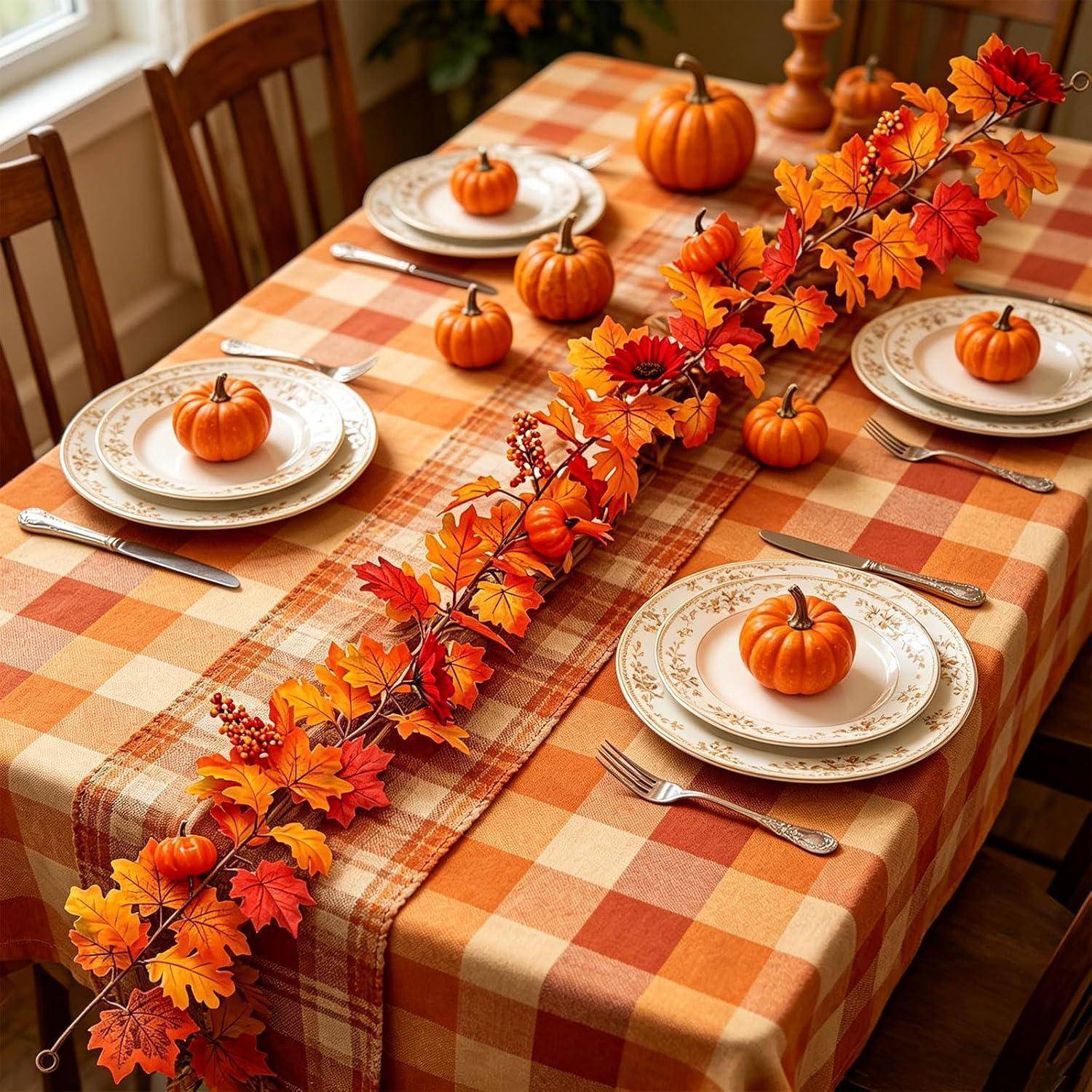 Herbstlich dekorierter Esstisch mit Karostoff, Herbstlaubgirlande und kleinen Kürbissen auf jedem Teller, hergerichtet für ein festliches Essen.