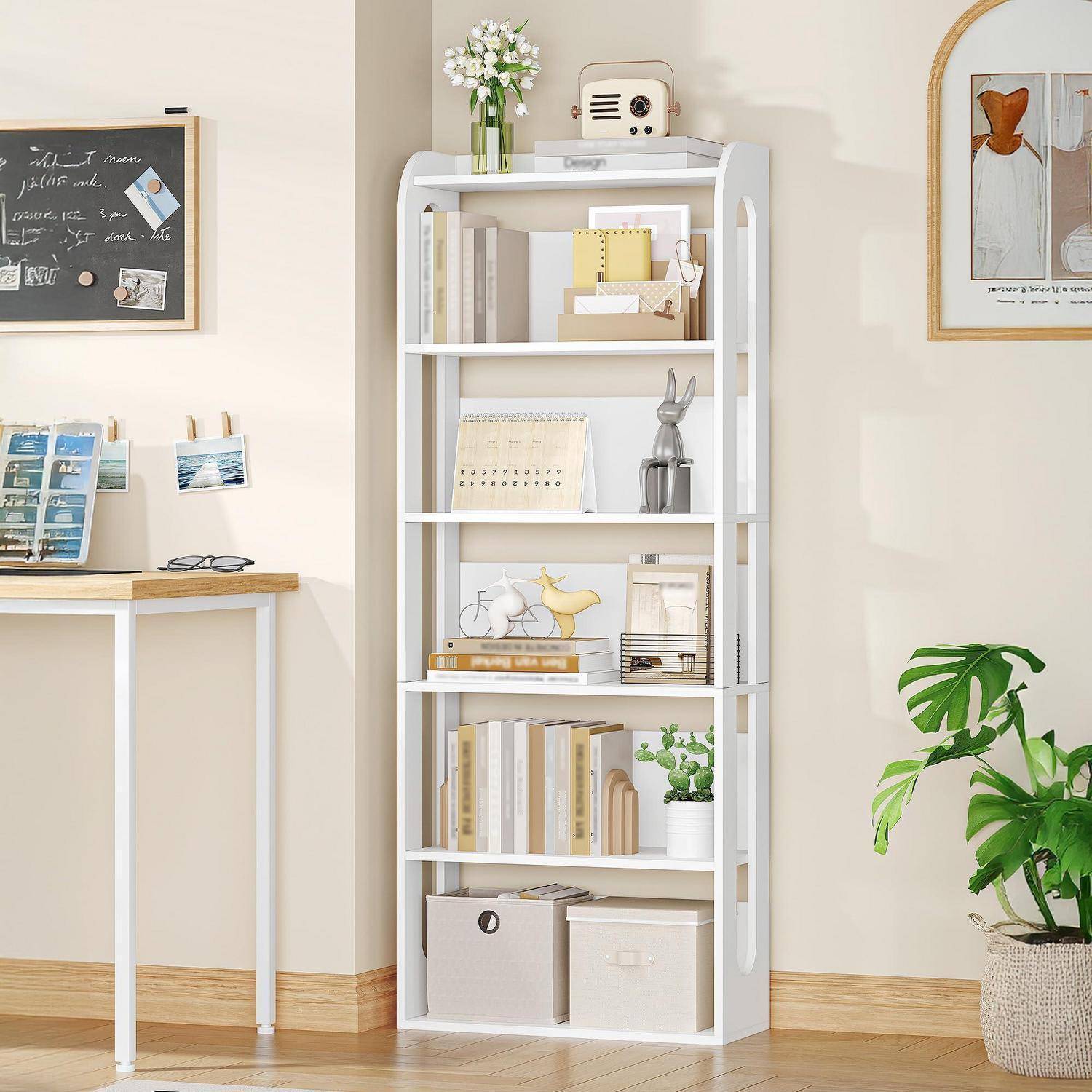 Weiß gestrichenes Bücherregal in einem minimalistischen Zimmer, gefüllt mit Büchern, Dekorationen, Blumen, einem kleinen Radio und Aufbewahrungsboxen neben einem Schreibtisch und einer Topfpflanze.