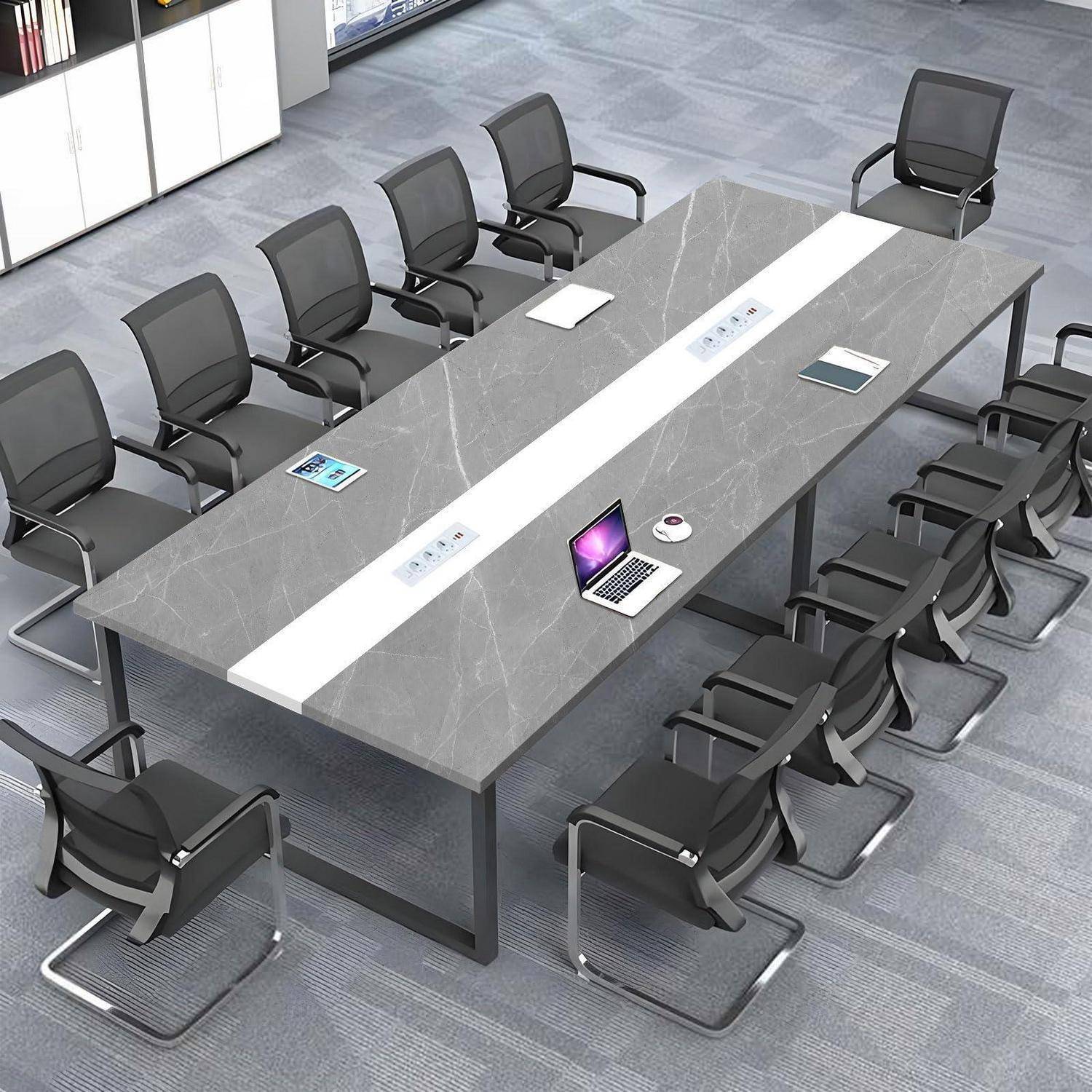 Moderner Konferenzraum mit einem langen grauen Konferenztisch, umgeben von schwarzen Bürostühlen; ein Laptop, ein Notizblock und eine Tasse stehen auf dem Tisch.