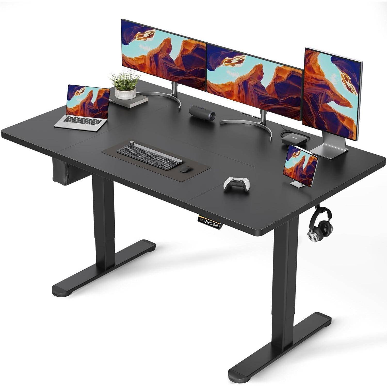 Schwarzer Stehschreibtisch mit drei Monitoren, Laptop, Tastatur, Maus, Game-Controller, Telefon, Kopfhörern, Webcam und kleiner Pflanze, angeordnet in einem sauberen Arbeitsplatz-Setup.