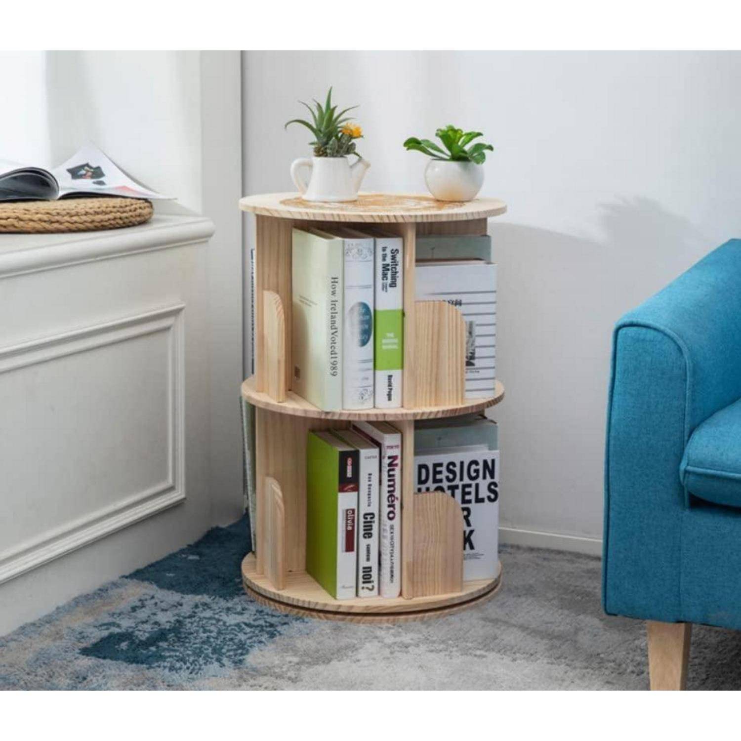Rundes hölzernes Bücherregal mit Büchern und zwei kleinen Topfpflanzen neben einem blauen Sofa in einem hellen Raum.