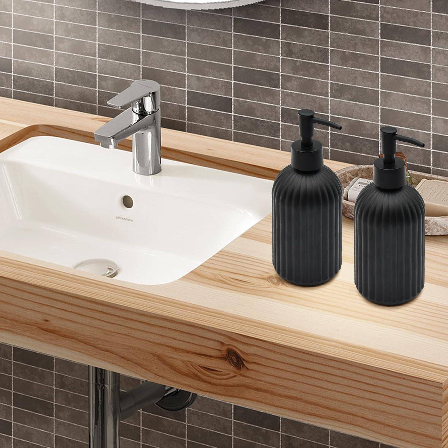 Modernes Badezimmer-Waschtisch mit weißem Waschbecken, verchromtem Wasserhahn und zwei schwarzen Seifenspendern auf einer hellholzfarbigen Arbeitsplatte vor grauem Fliesenbelag.