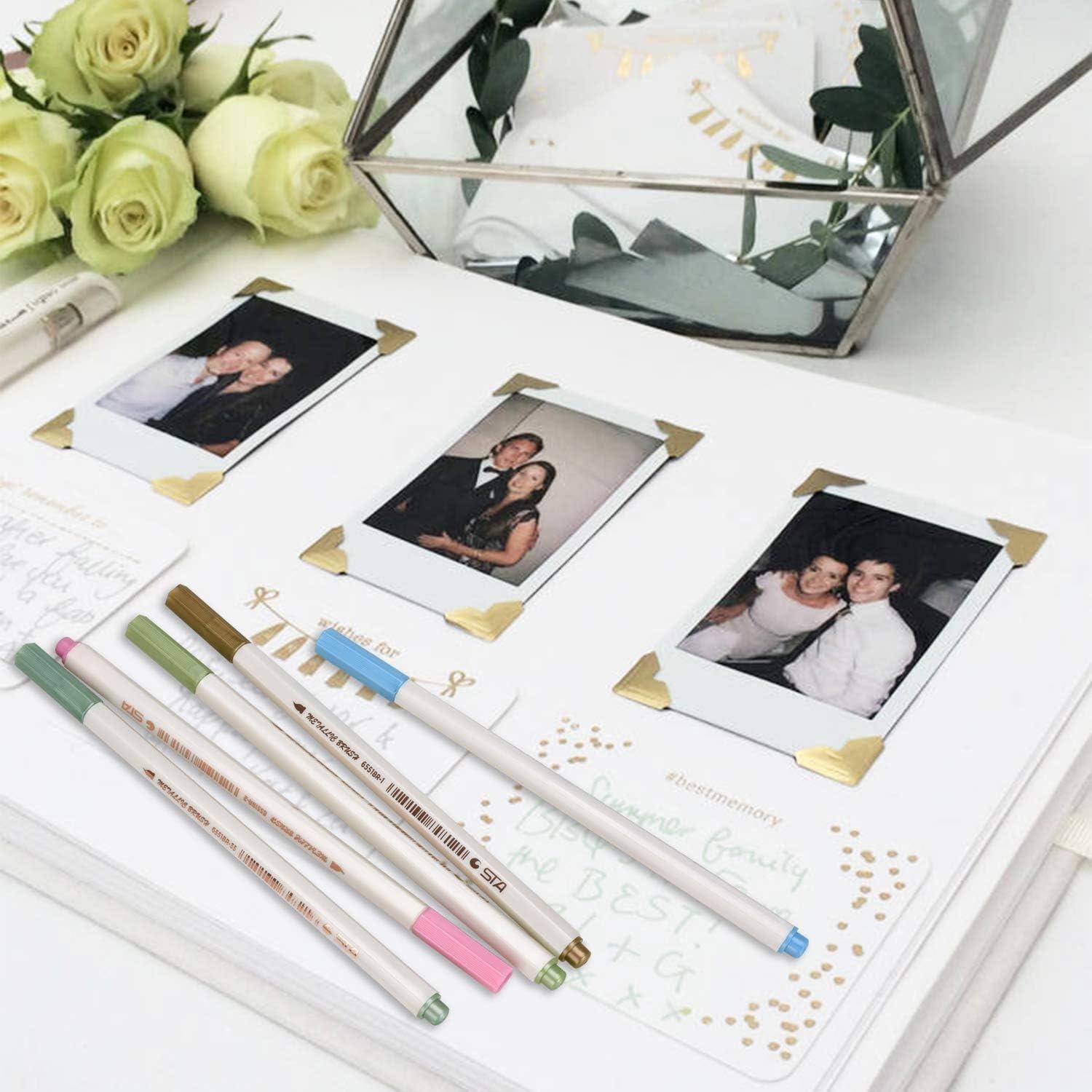 Eine dekorierte Hochzeitsgästebuchseite mit drei geklebten Polaroid-Fotos und mehreren Stiften, arrangiert neben weißen Rosen und einer gläsernen geometrischen Vase.