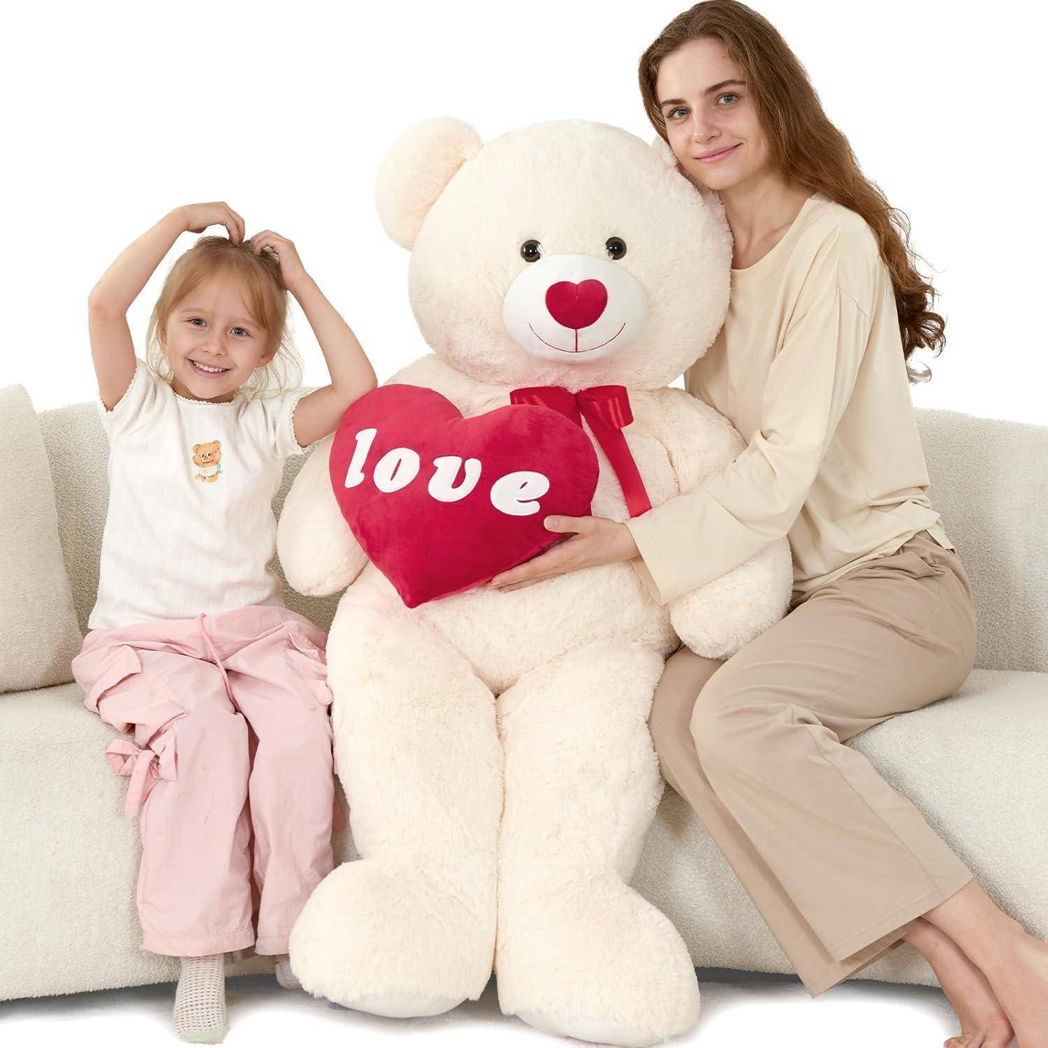 Eine Frau und ein junges Mädchen sitzen auf einem Sofa mit einem großen Teddybär, der ein rotes Herz hält, auf dem „Liebe