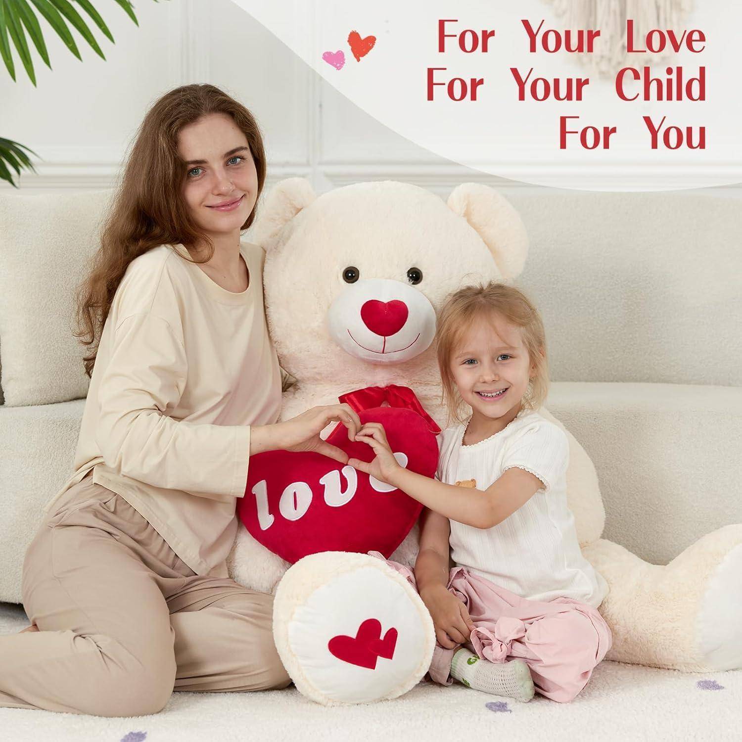 Mutter und Tochter sitzen mit einem riesigen Teddybären, der ein rotes „Ich liebe dich
