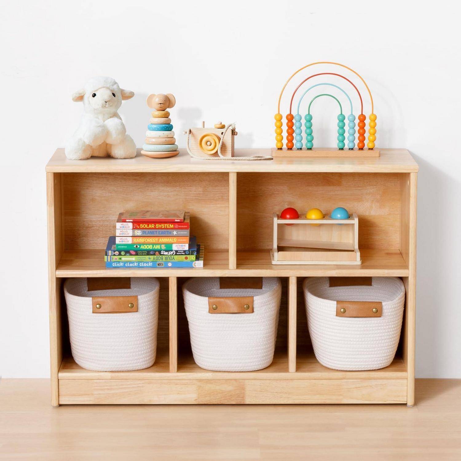 Ein Holzregal mit Spielzeugen, gestapelten Kinderbüchern und drei weißen Aufbewahrungskörben, angeordnet als ordentlicher Kinderzimmer-Organizer.