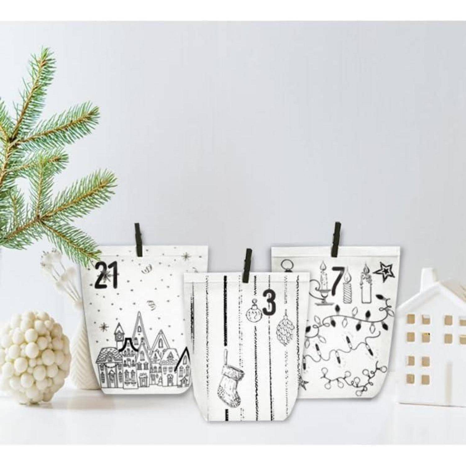 Drei hängende Weihnachts-Adventskalender-Taschen mit den Nummern 21, 3 und 8 mit festlichen Weihnachtskritzeleien auf einem weißen Regal, neben Dekoration und Tannenzweigen.