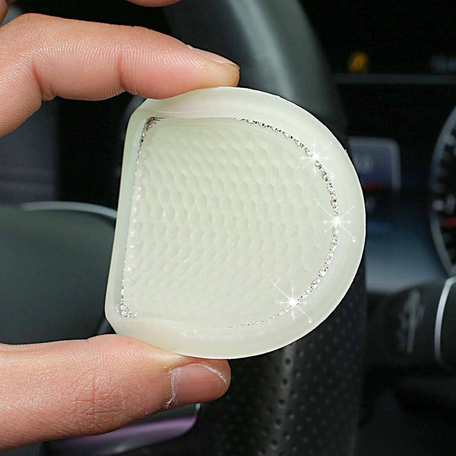 Eine Hand hält ein durchsichtiges, gelartiges Silikonpad mit strukturierter Mitte und glitzerndem Rand, das sich im Auto befindet.
