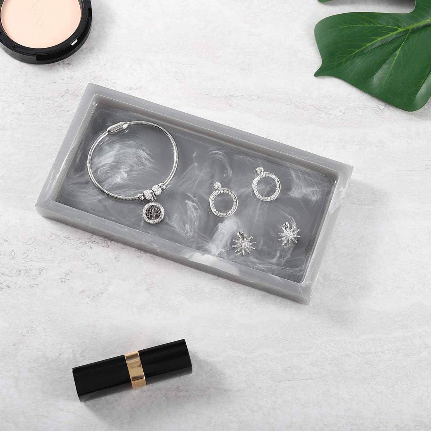 Geschenkbox mit silbernem Armband und Ohrrings, dargestellt neben einem Lippenstift auf einer hellen Oberfläche mit grünem Blatt