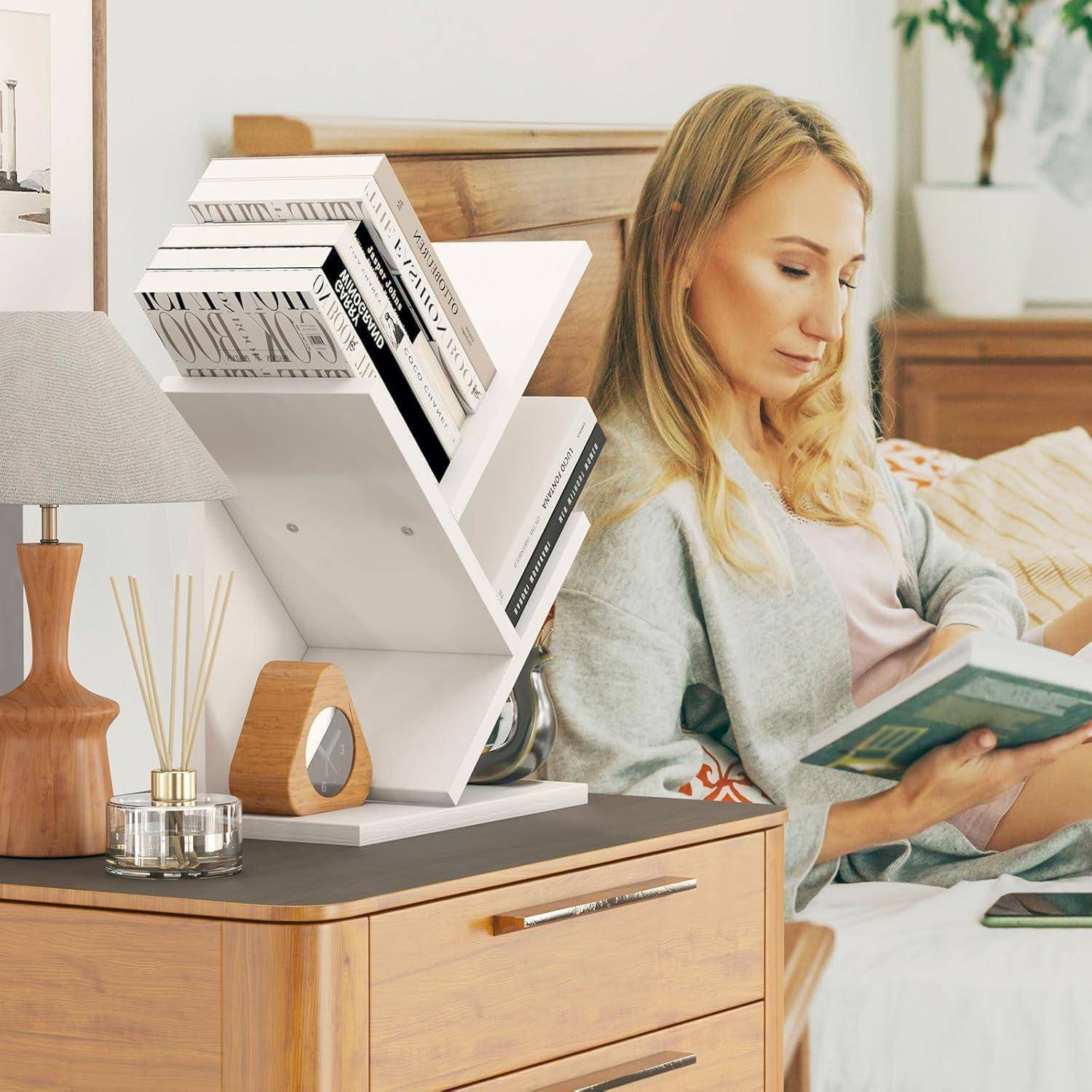 Blonde Frau sitzt auf einem Bett und liest ein Buch neben einem weißen geometrischen Bücherregal und einem Nachttisch in einem hellen Schlafzimmer.