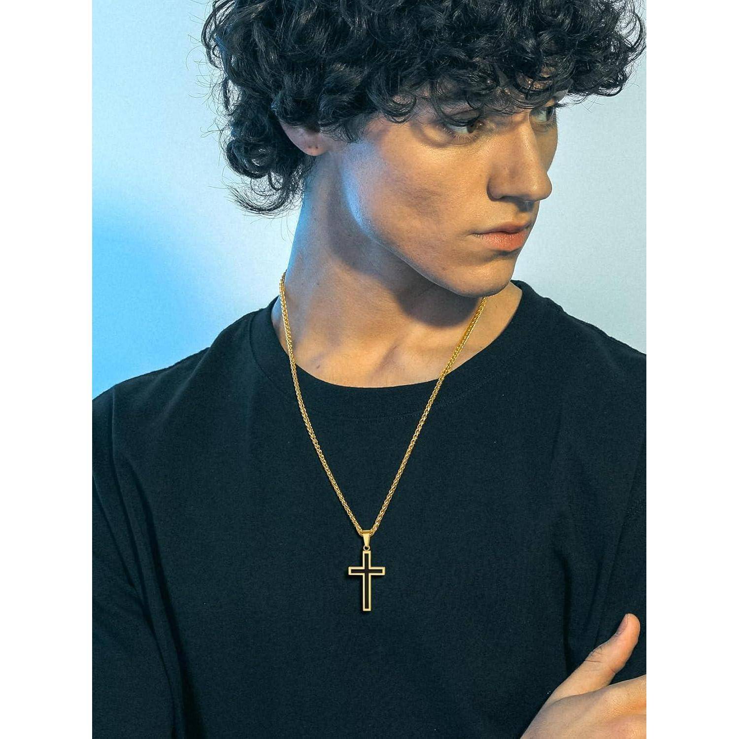 Porträt eines jungen Mannes mit lockigem Haar, der ein schwarzes Hemd und eine goldene Kreuzkette trägt, blickt zur Seite vor einem blauen Hintergrund.
