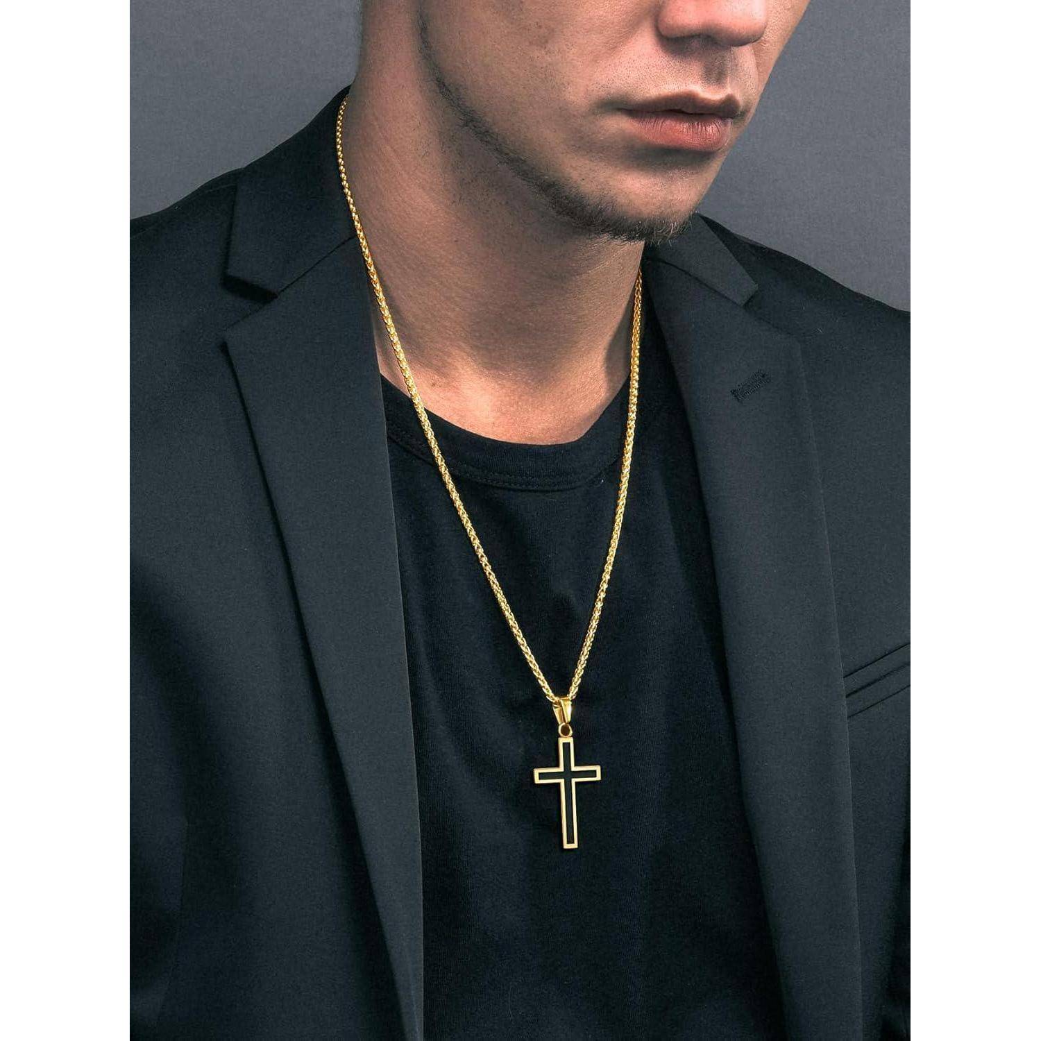 Nahaufnahme eines Mannes in einem schwarzen Blazer und Hemd, der eine goldene Kreuzkette um den Hals trägt, vor einem grauen Hintergrund.