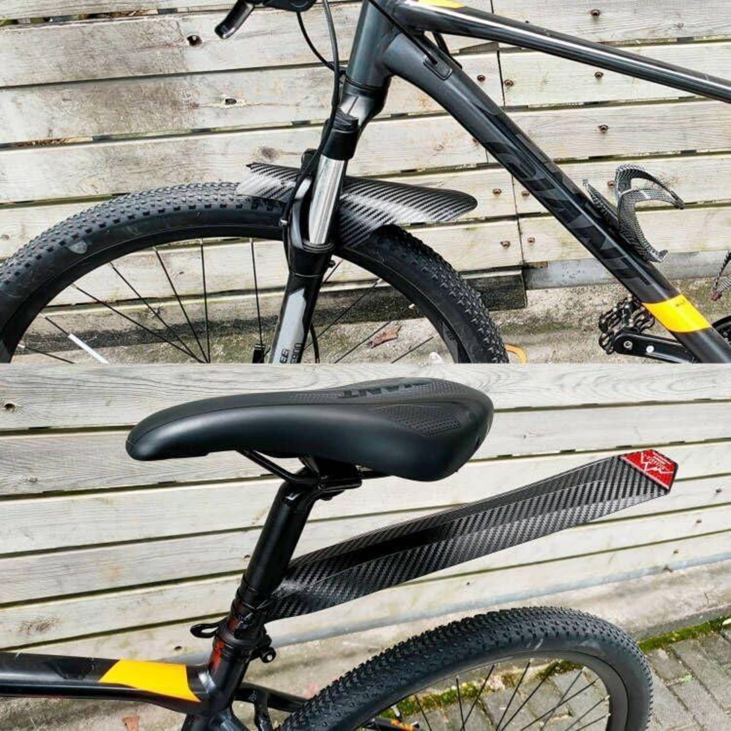 Nahaufnahme eines schwarzen Mountainbikes mit dem Vorderrad, dem Rahmen und dem Sattel vor einem weißen Holzzaun.
