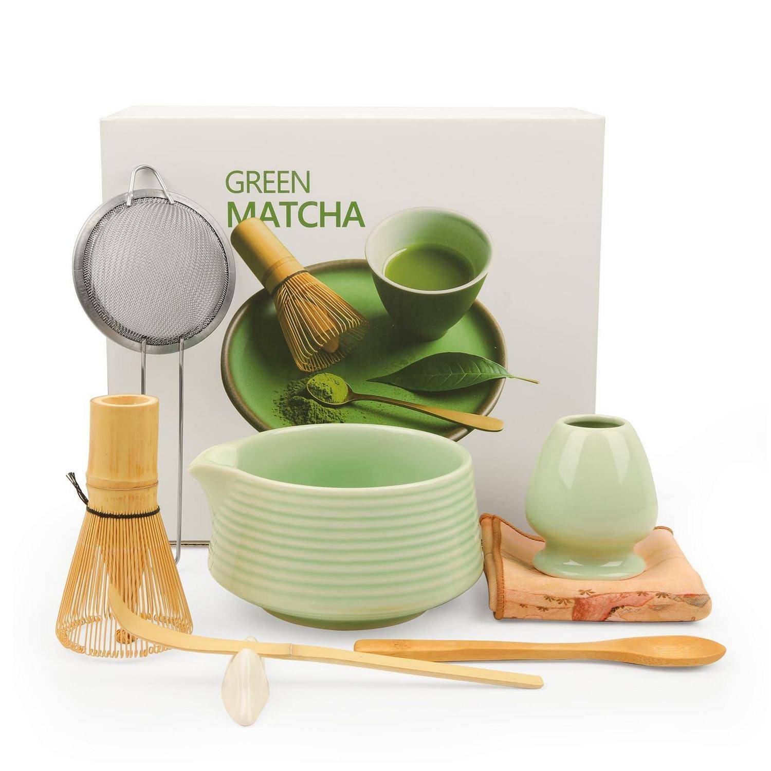 Matcha-Tee-Set-Display mit Schüsseln, Schneebesen, Löffel, Sieb und grünen Keramiktassen sowie Zubehör auf weißem Hintergrund.