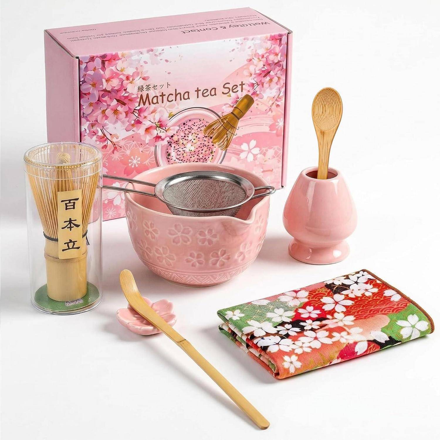 Rosafarbenes Matcha-Tee-Set mit Schachtel, Schneebesen, Siebschale, Bambuslöffel, Löffelhalter, Teelöffel und Blumentuch auf weißem Hintergrund.
