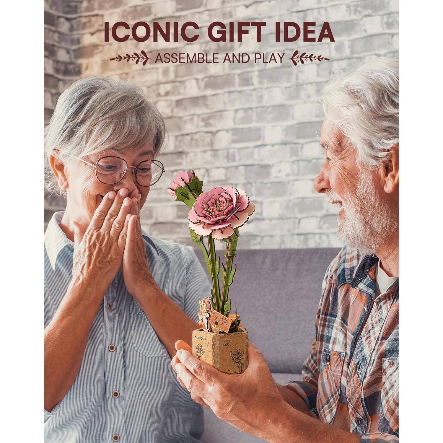 Ein älterer Mann überreicht einer überraschten älteren Frau ein handgefertigtes Blumengeschenk; der Text lautet „IKONISCHE GESCHENKIDEE