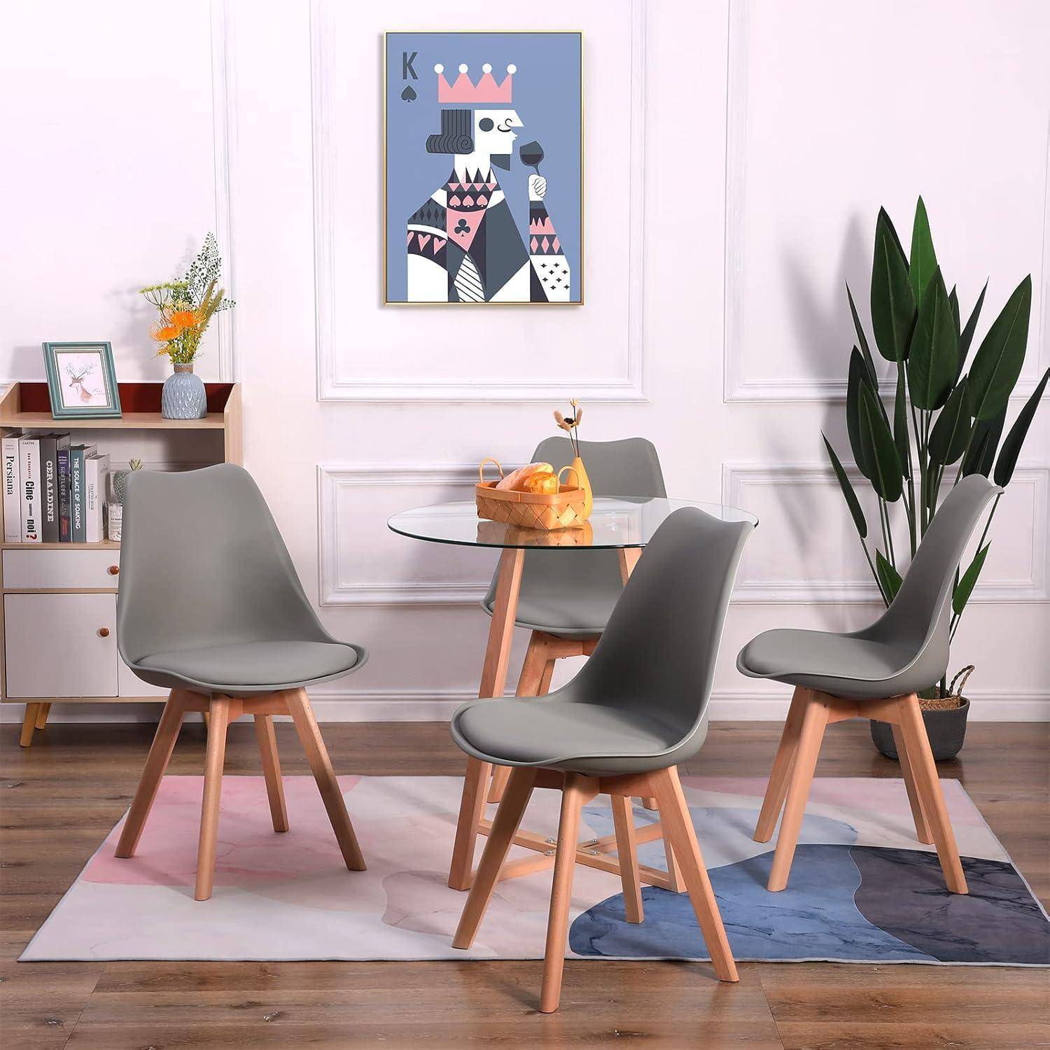 Moderne Essecke mit vier grauen Stühlen um einen Glastisch auf einem Pastellteppich, neben einer Pflanze und Wandkunst.