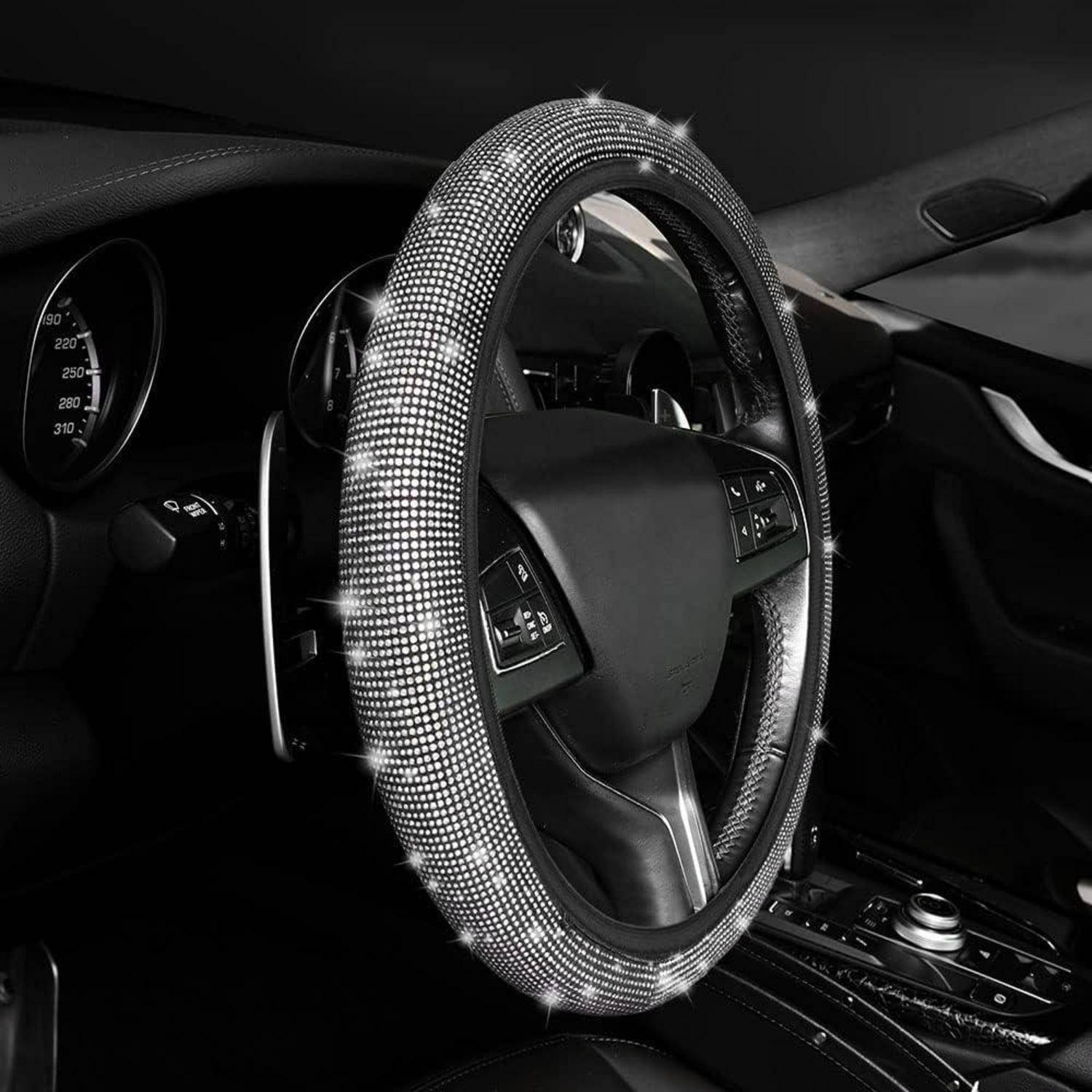 Nahaufnahme des Innenraums eines Autos mit einem Lenkrad, das mit glitzernden Strass-Steinen bedeckt ist, und beleuchteten Armaturenbrettknöpfen.
