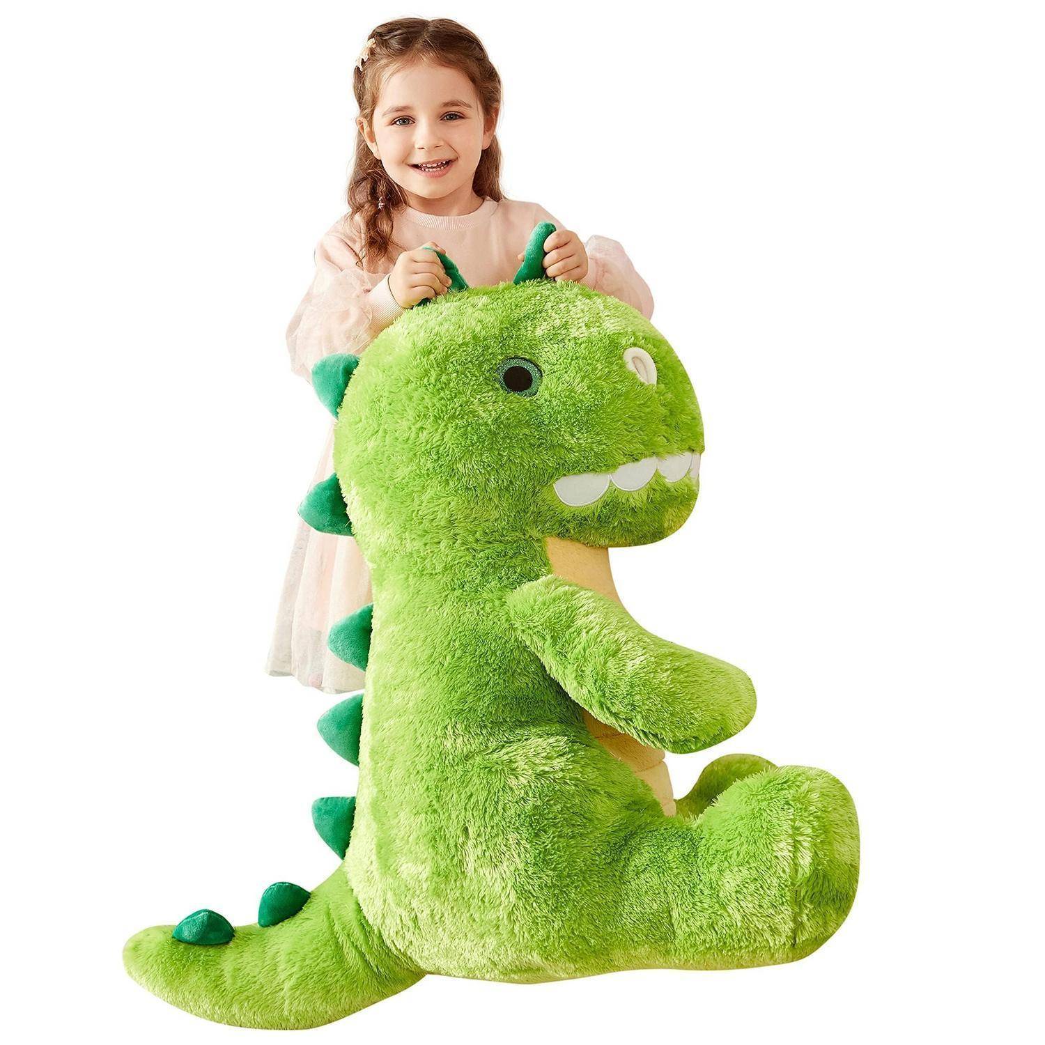 Lächelndes junges Mädchen, das ein großes grünes Dinosaurier-Plüschtier auf weißem Hintergrund umarmt.