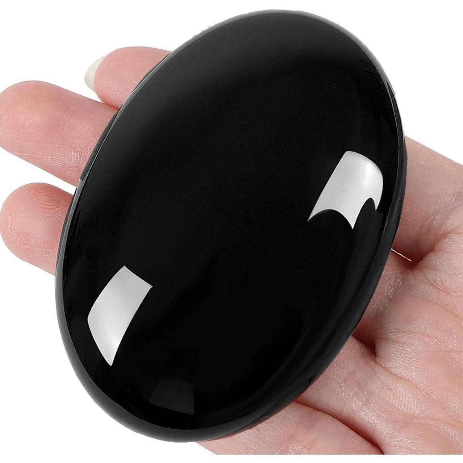 Eine Hand, die einen glatten schwarzen ovalen Stein oder ein poliertes Edelstein gegen einen weißen Hintergrund hält.