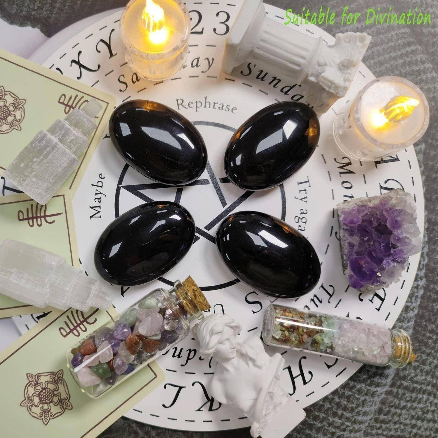 Dekorative spirituelle Ausstellung von vier schwarzen Steinen auf einer Wahrsagetafel, umgeben von Kerzen, Kristallflaschen, Amethyst und kleinen Figuren.
